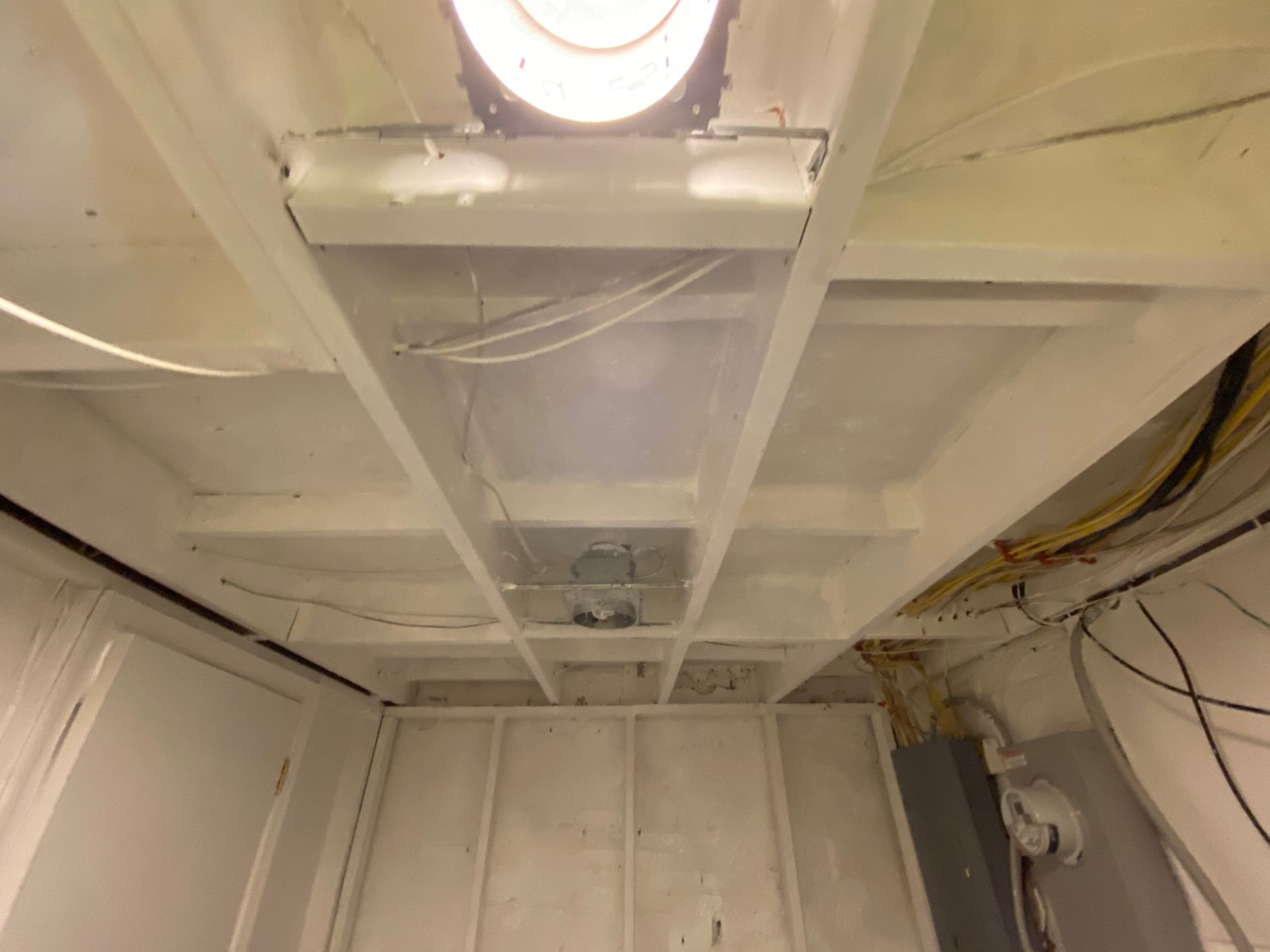 White ceiling with beams, lights, and wires in a room.