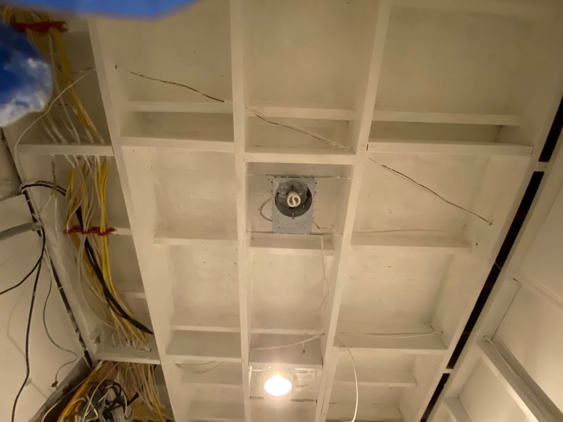 White grid ceiling with exposed wiring, a light fixture, and a fan.
