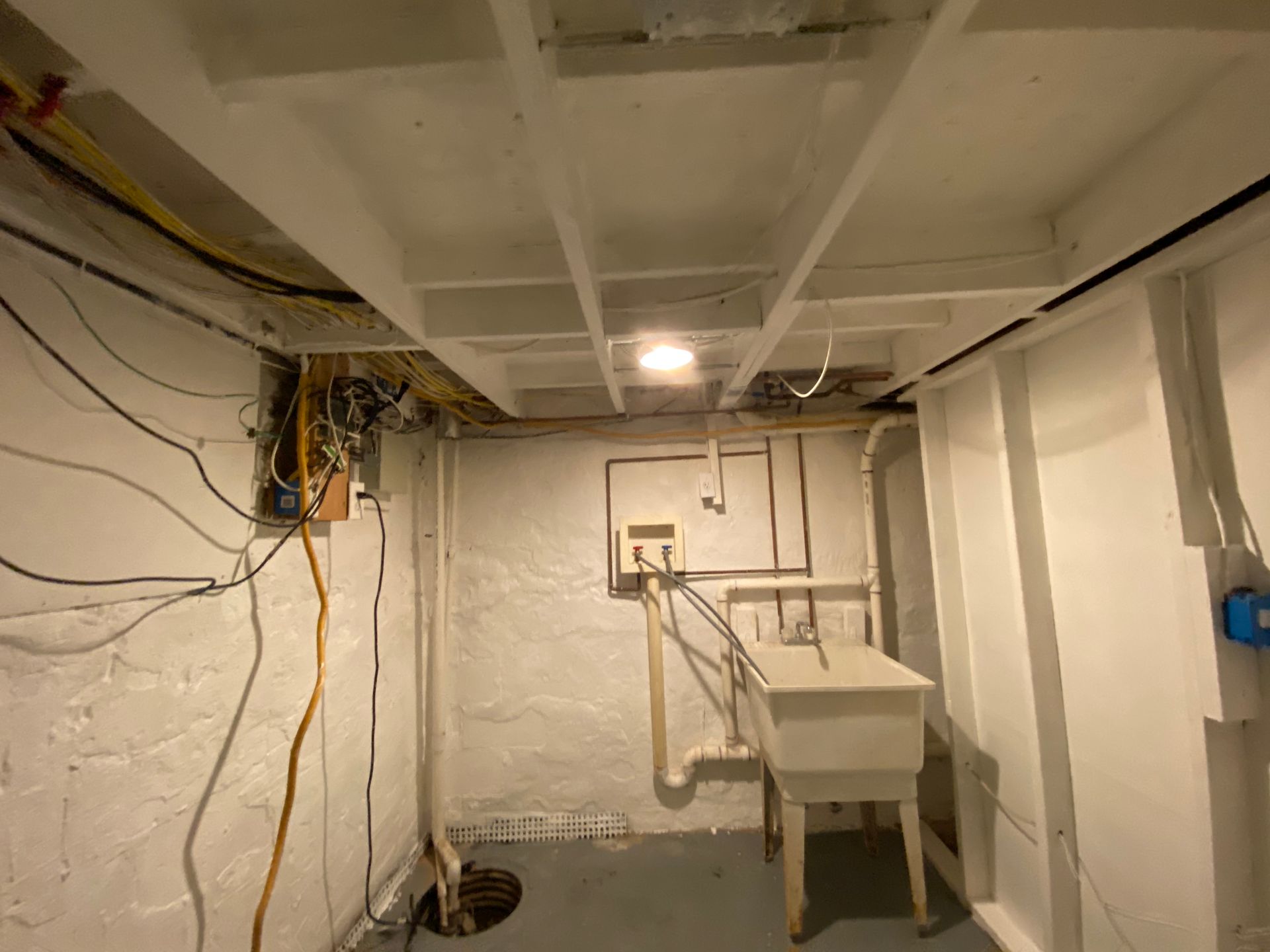 Basement utility room with exposed beams and wiring, a utility sink, and a drain on the floor.