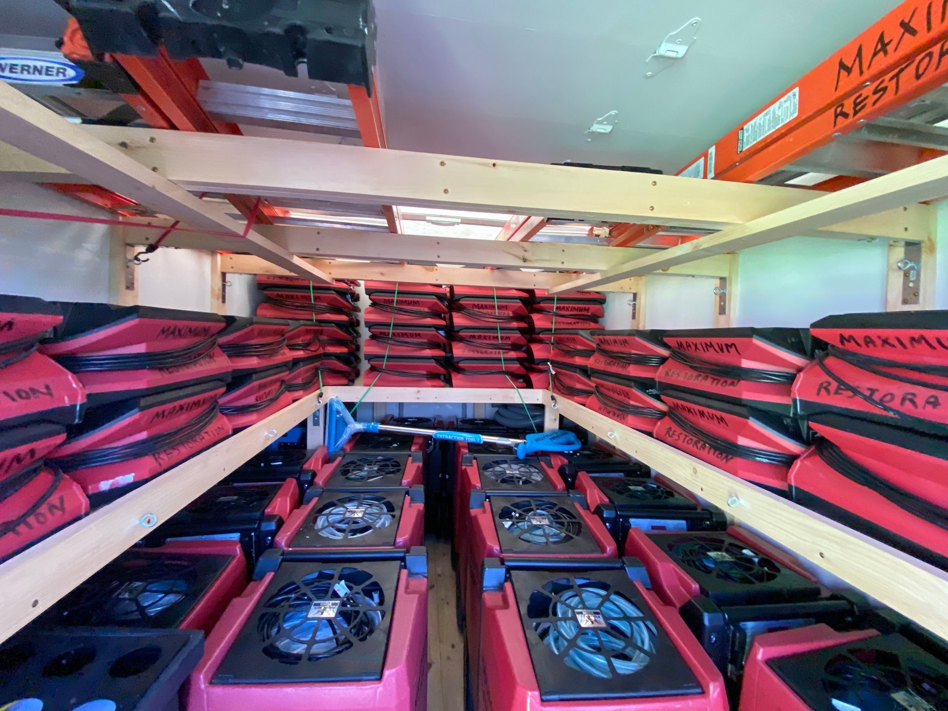 Rows of red and black industrial air movers and stacked equipment in a storage area.