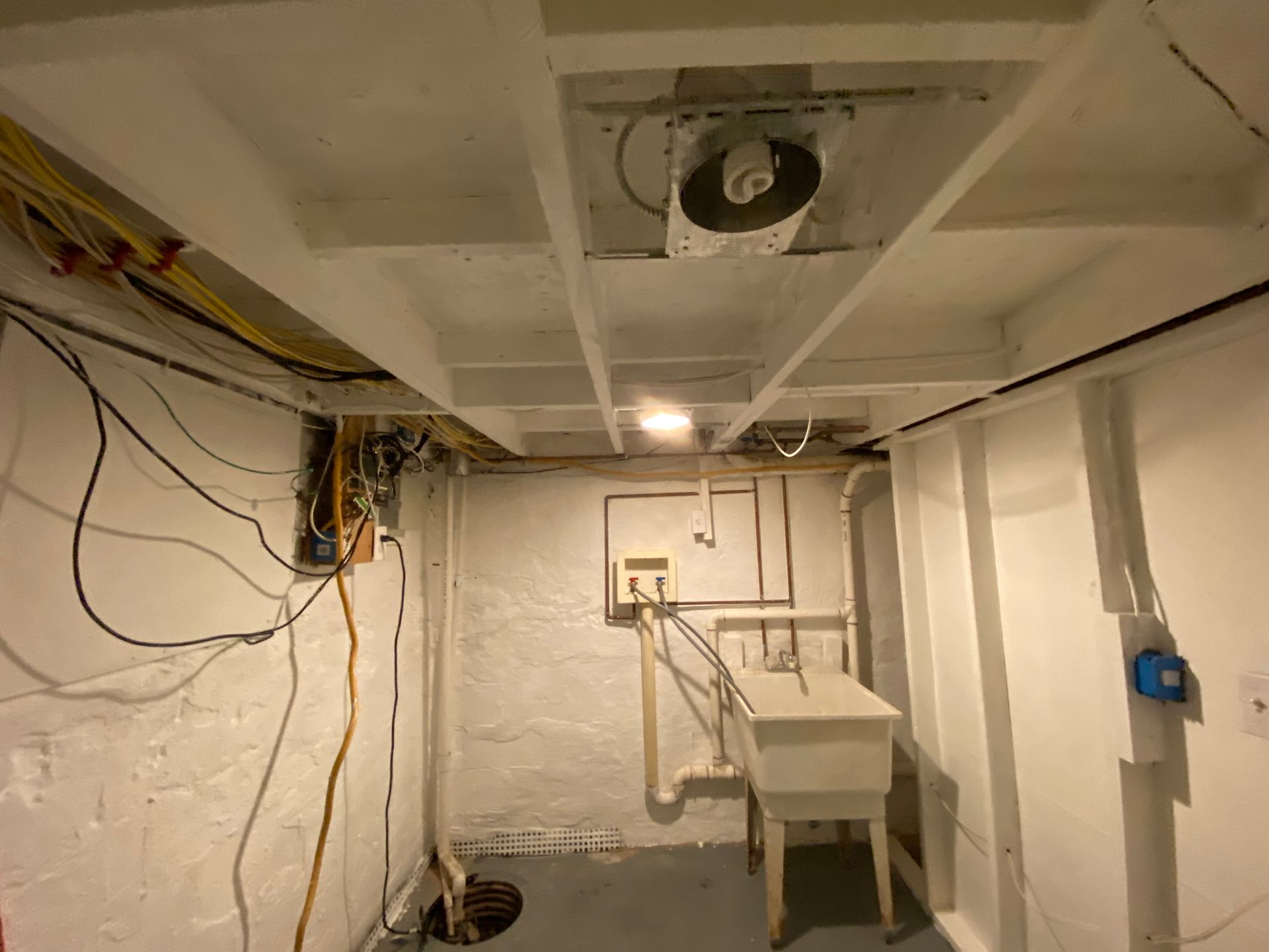Basement interior with exposed beams, electrical wiring, utility sink, and white walls.