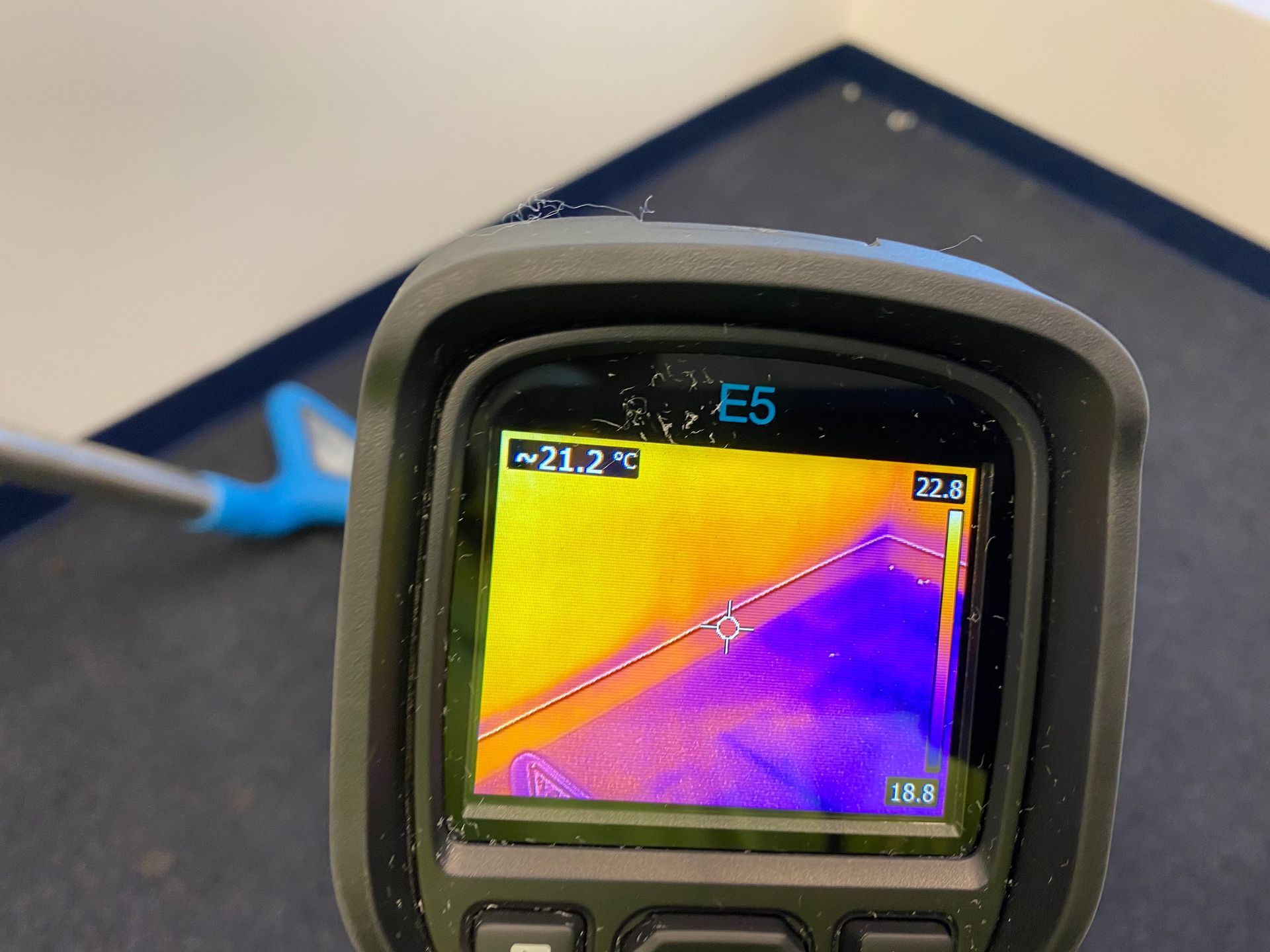 Thermal camera displaying temperature variations on a corner, with a blue and gray device visible.