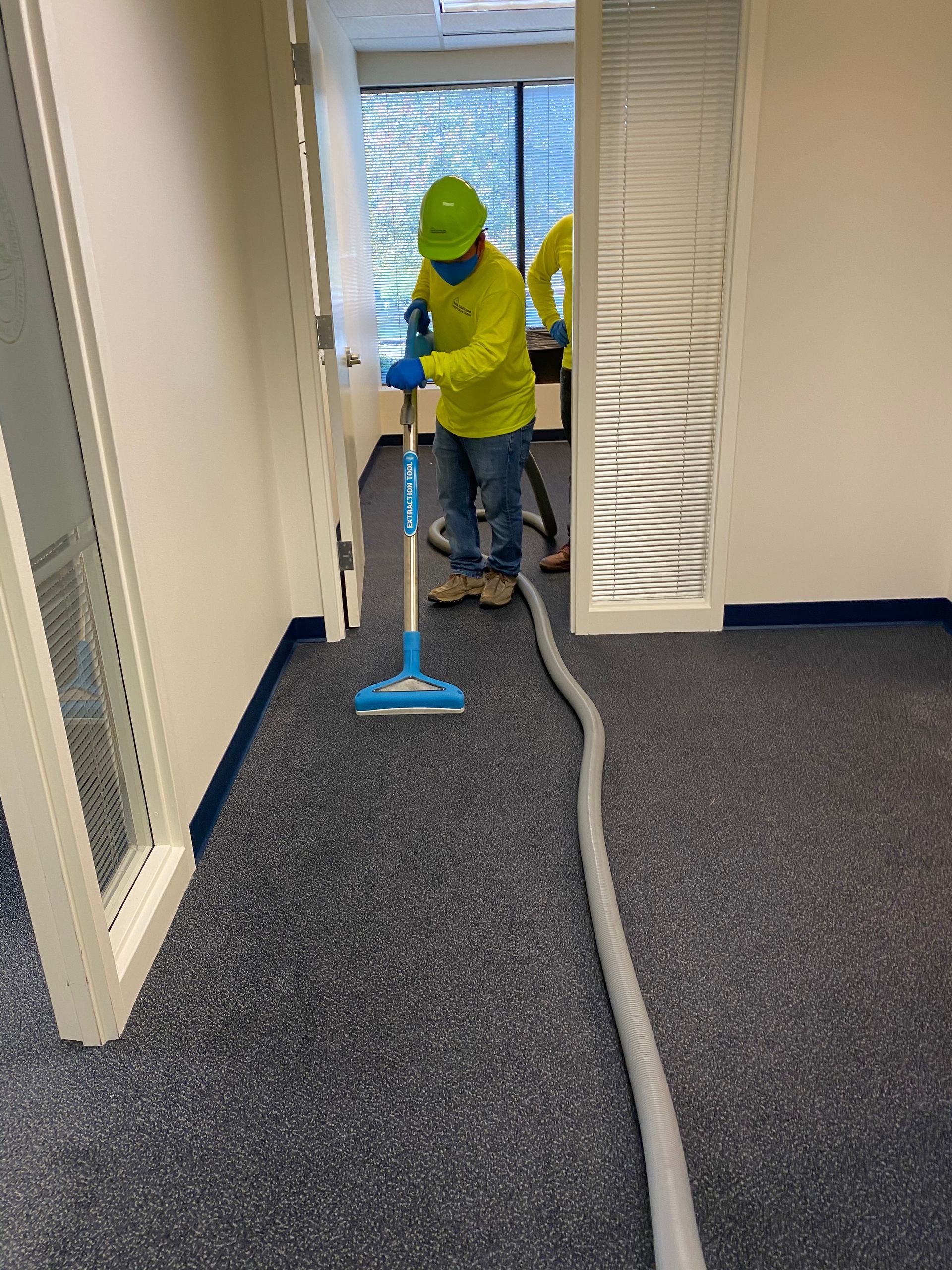 Person in yellow shirt and hard hat vacuuming carpeted office floor.