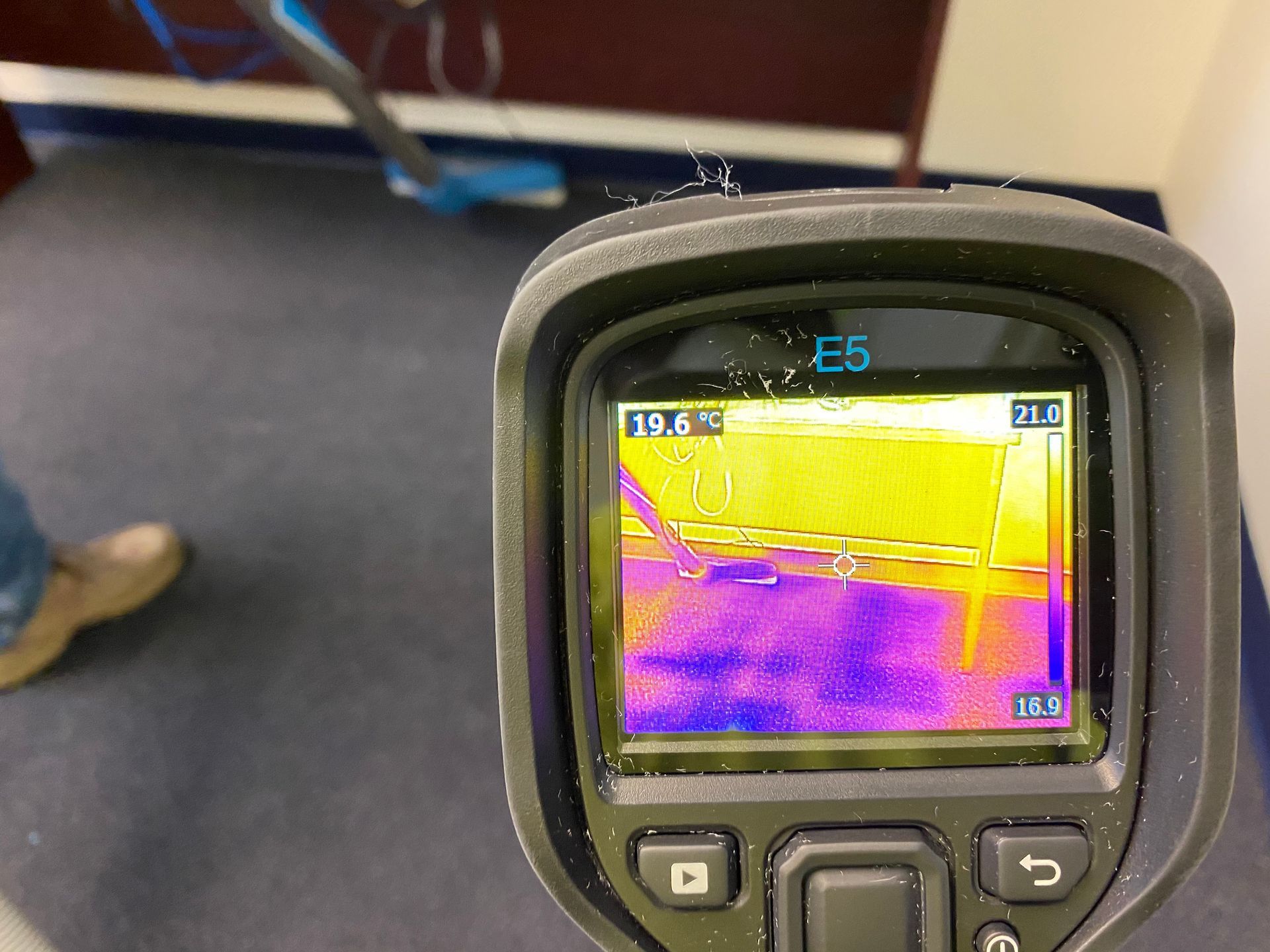 Thermal camera displaying a heat map of a wall. The device is held by a person.