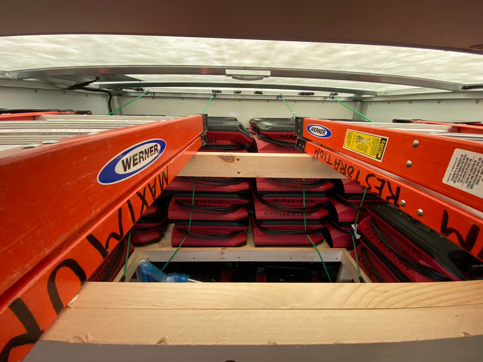 Orange ladders stacked above a compartment filled with red tool bags, inside a vehicle.