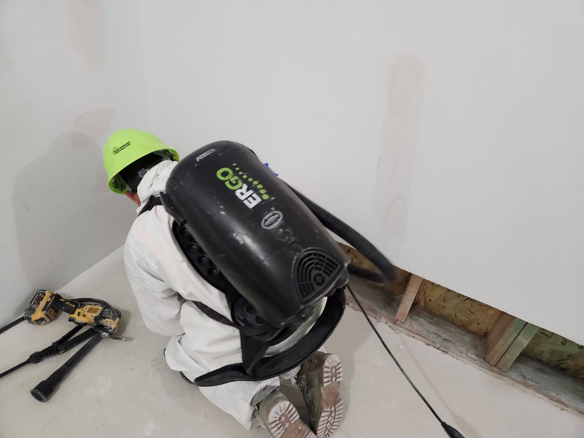 Construction worker wearing backpack vacuum cleaning wall corner.