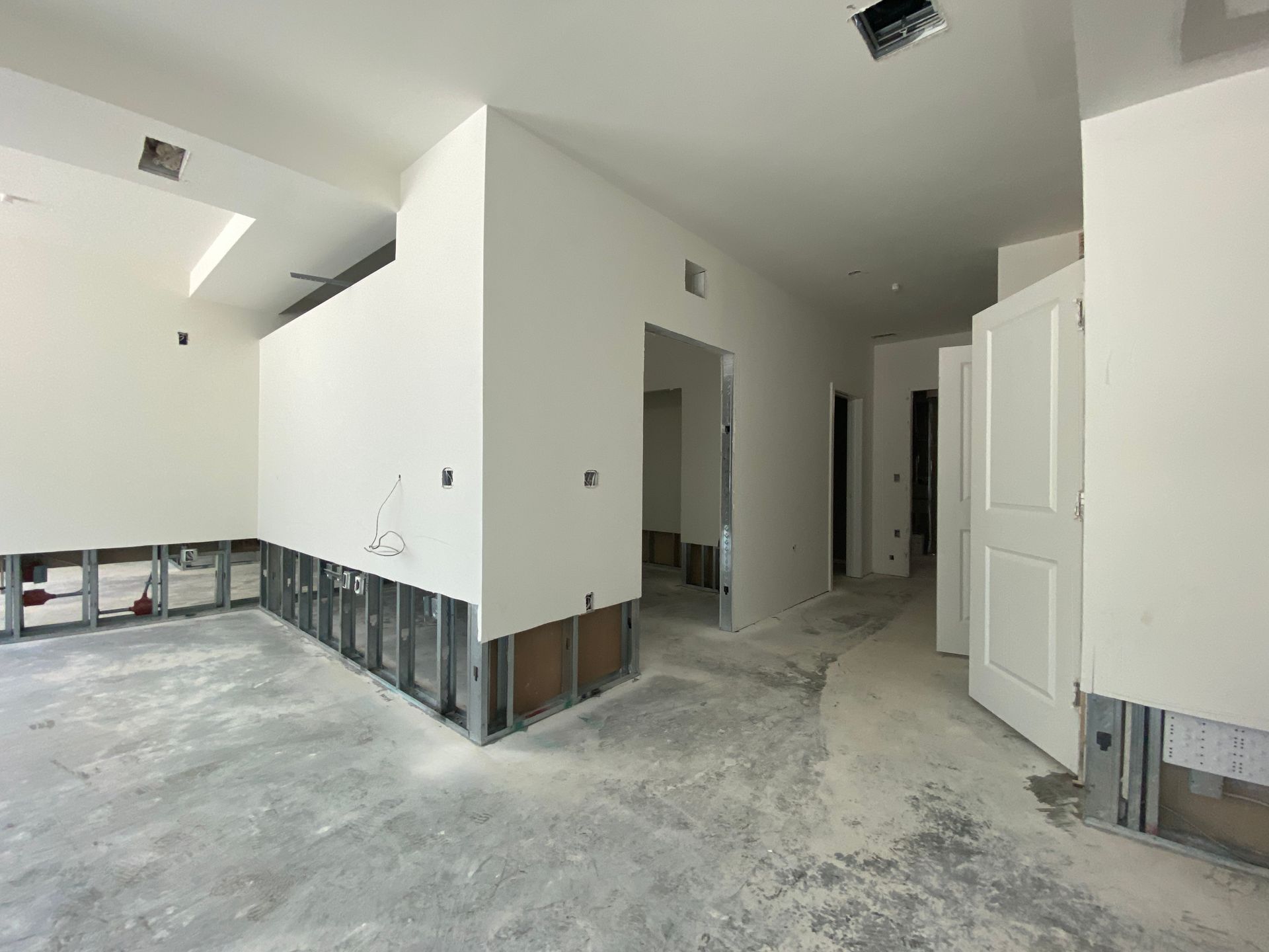 Interior view of a building under construction, showing drywall walls, exposed framing, and concrete floors.