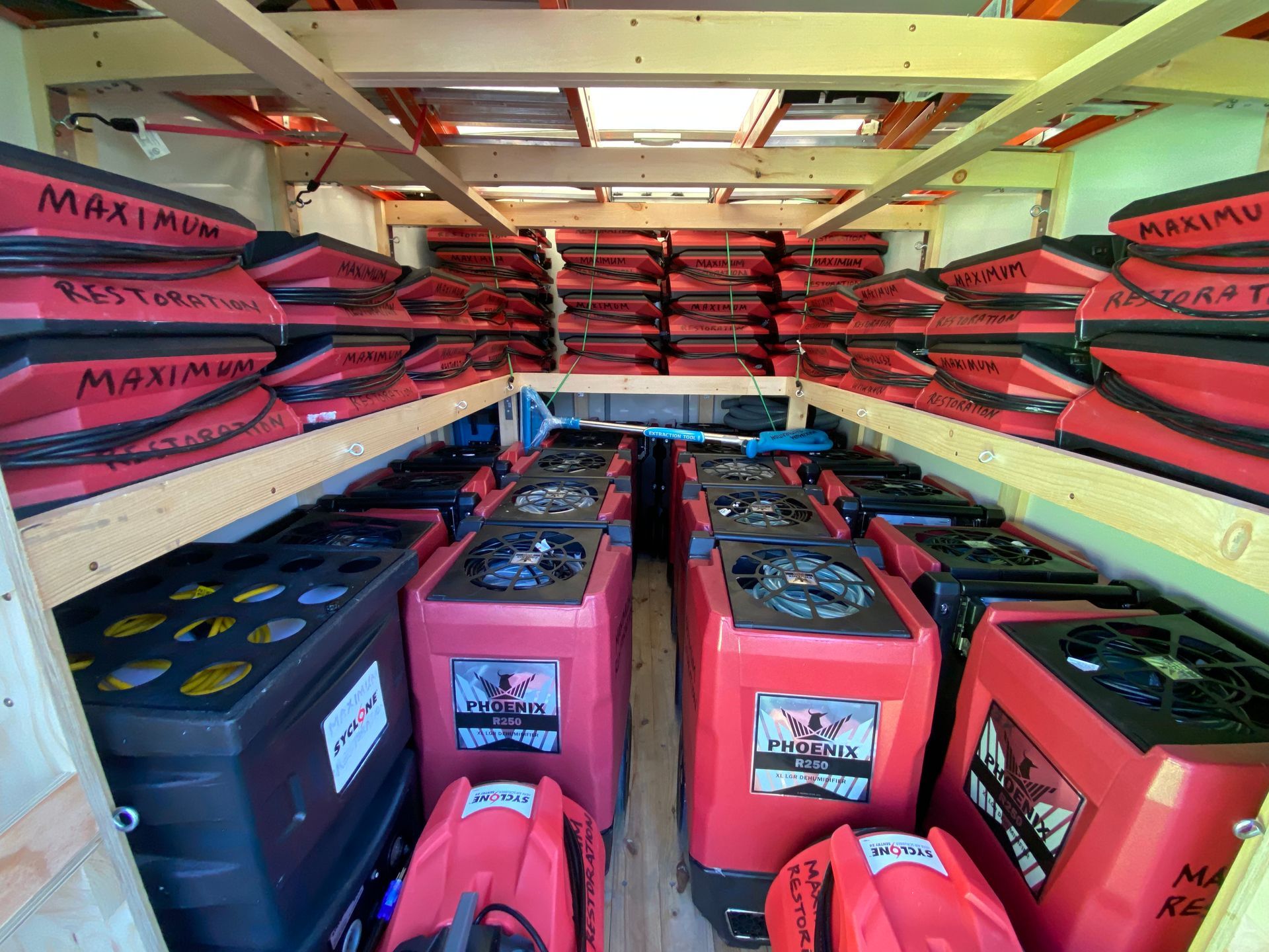 Red and black equipment stacked inside a wooden enclosure; fans and dehumidifiers.