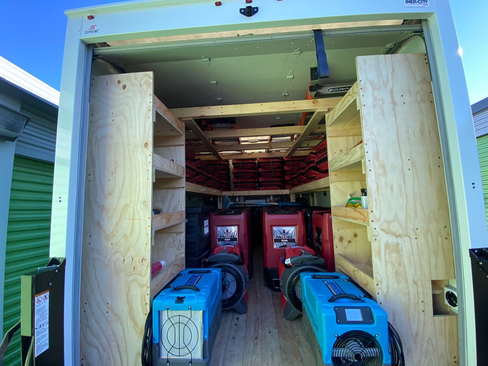Interior of a white trailer, with plywood shelves and several welding machines.