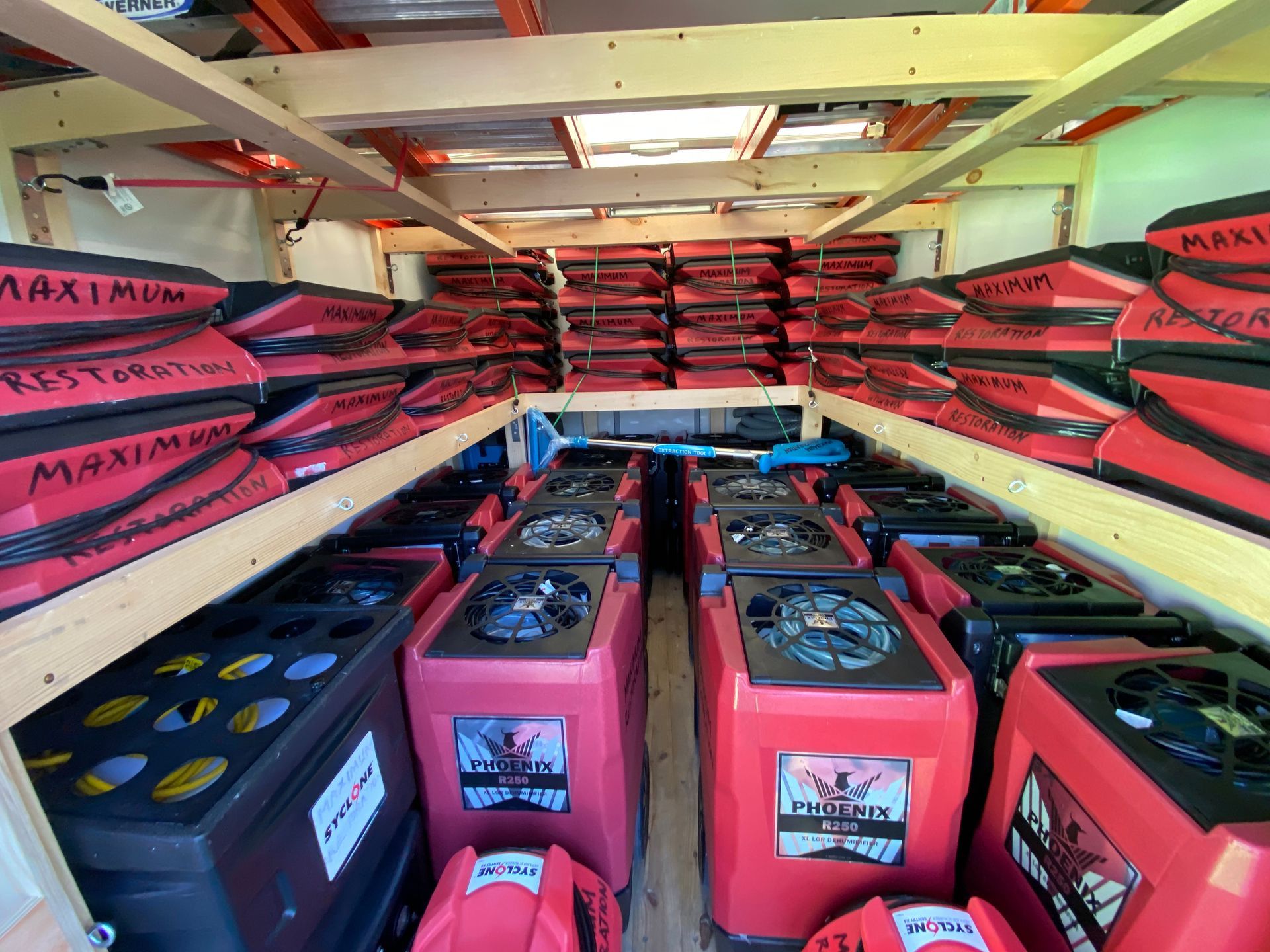 Interior view of a storage area filled with red and black equipment and stacked items, possibly restoration supplies.