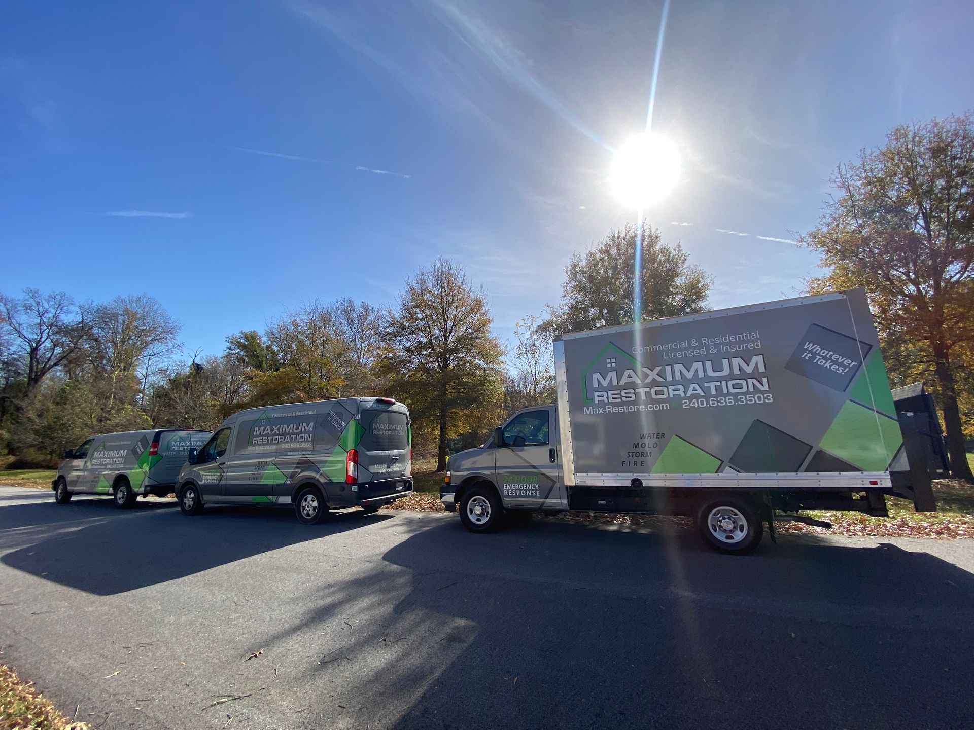 Three branded vans parked on a road with a bright sun overhead. 