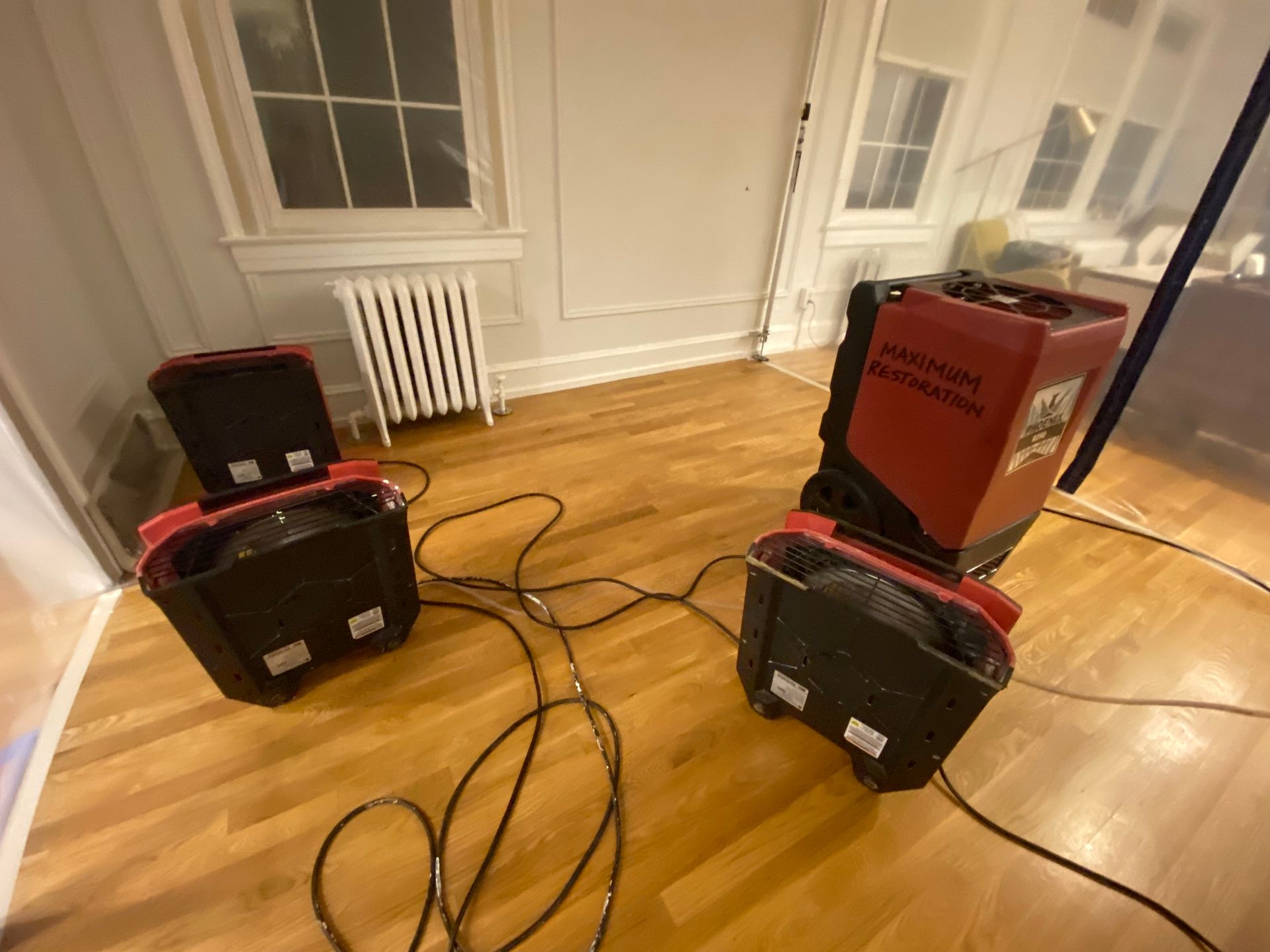 Two red industrial dehumidifiers on wood floor in a room, with electrical cords visible.