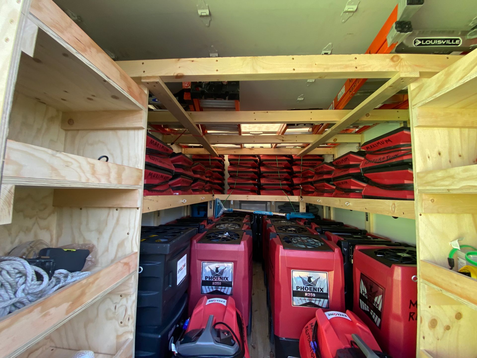 Interior view of a van filled with equipment. Shelves hold red bags, black boxes, and red machines.