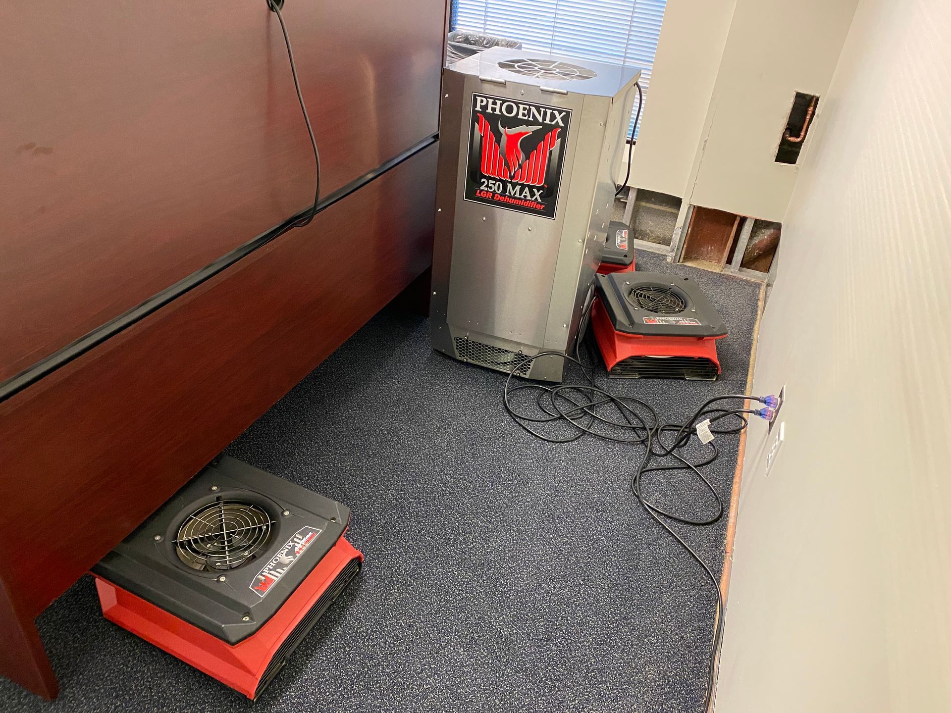 Dehumidifiers on carpet near a desk, and a wall with holes in it.