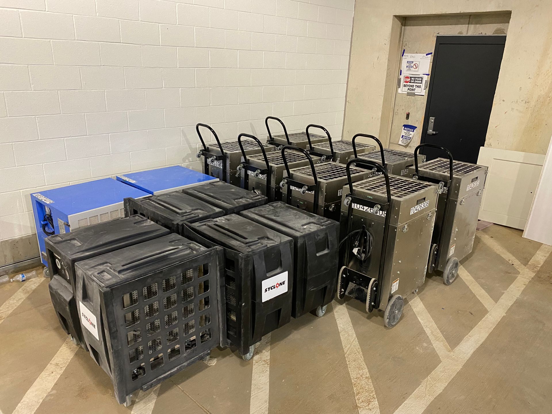 A collection of black and blue storage boxes and carts with handles and wheels, in a storage area.