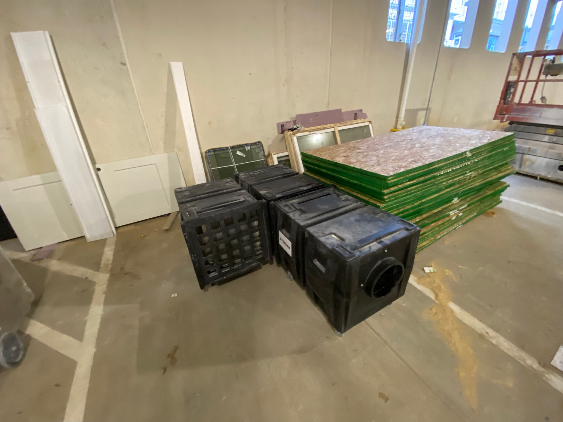 Black plastic crates and green boards stacked in a room with white walls and a concrete floor.