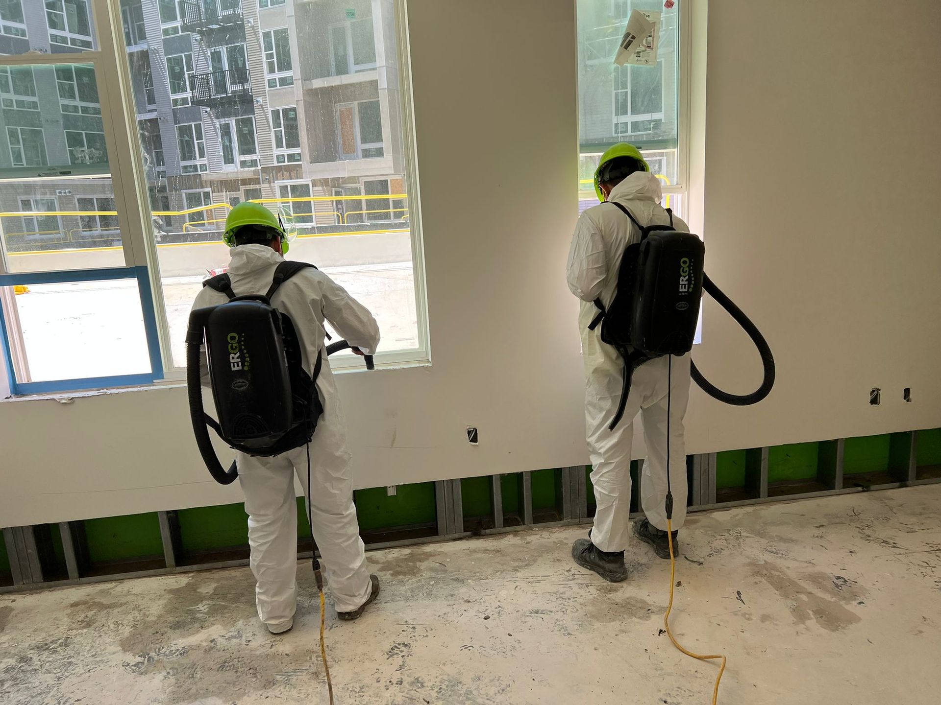 Two people in protective suits spraying walls in a building under construction.