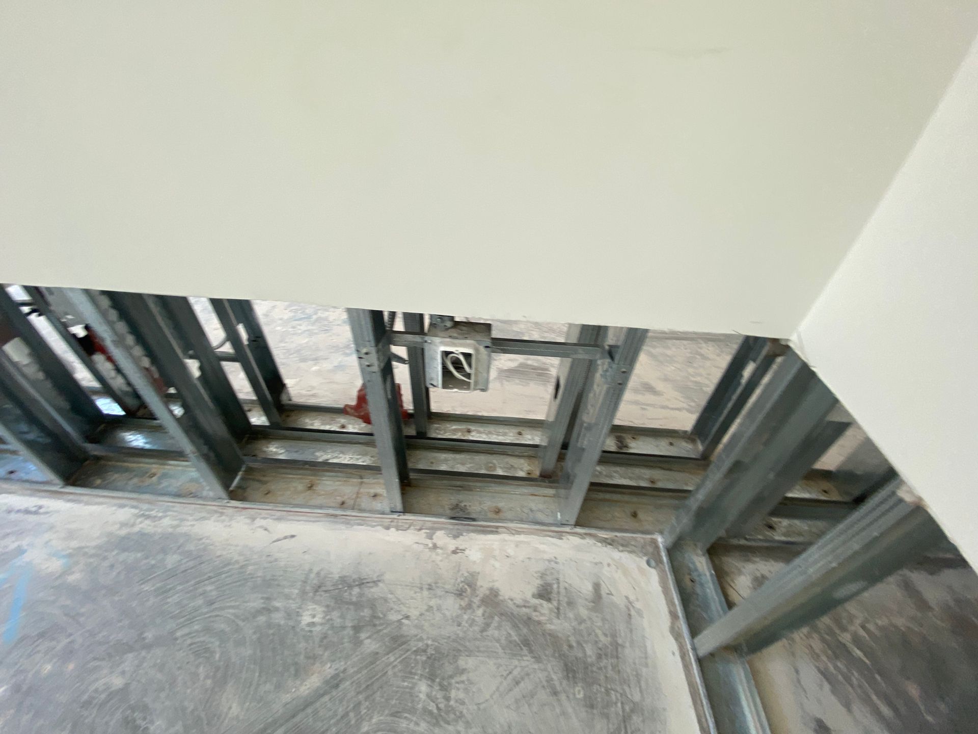Steel framing of a ceiling and walls with electrical box visible; gray concrete floor, white ceiling.