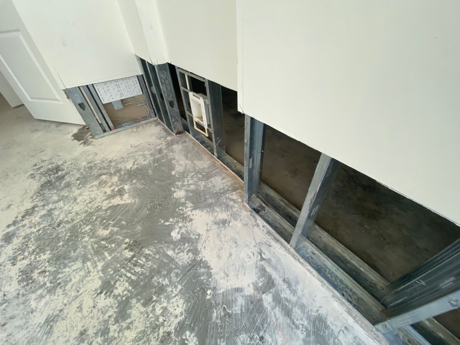 Interior view of a room under construction; exposed metal framing, unfinished walls, and concrete floor.