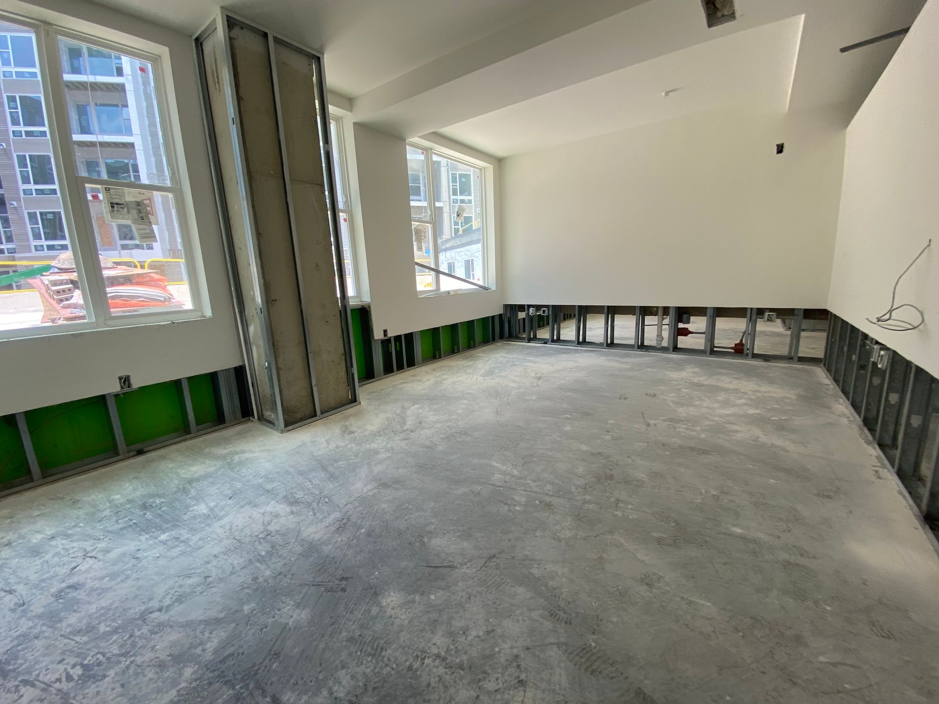 Interior construction: Room with exposed metal framing, concrete floor, windows, and partially installed walls.
