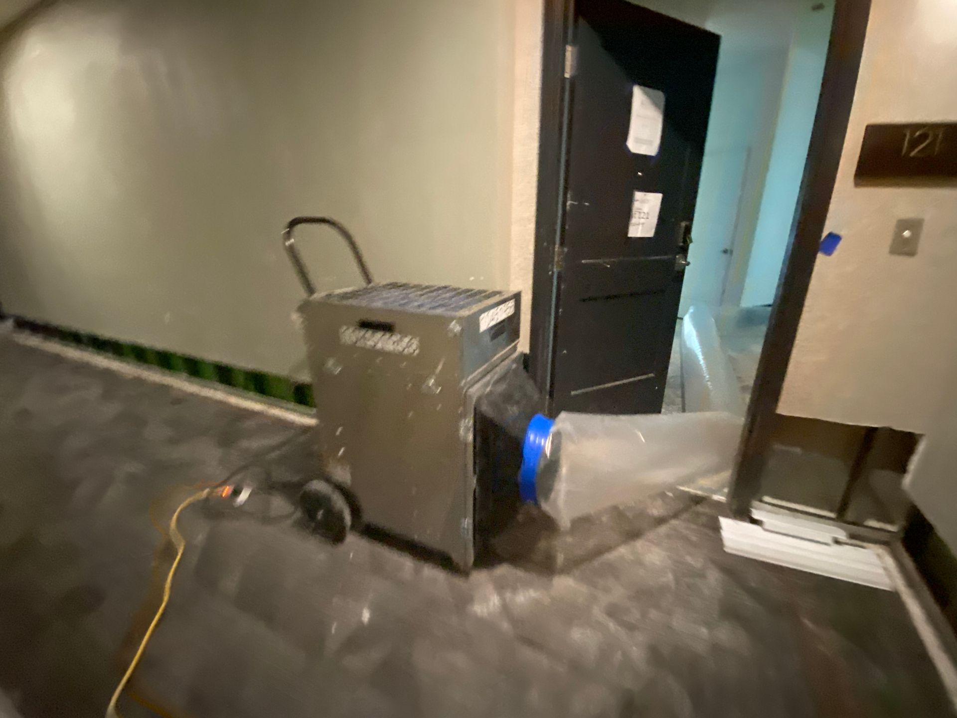 Dehumidifier in a hallway with a partly open door and plastic sheeting.