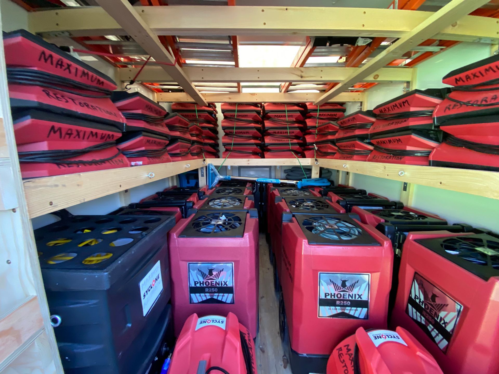 Inside a trailer, rows of red and black ventilation units and red-cased air movers are stacked on shelves.