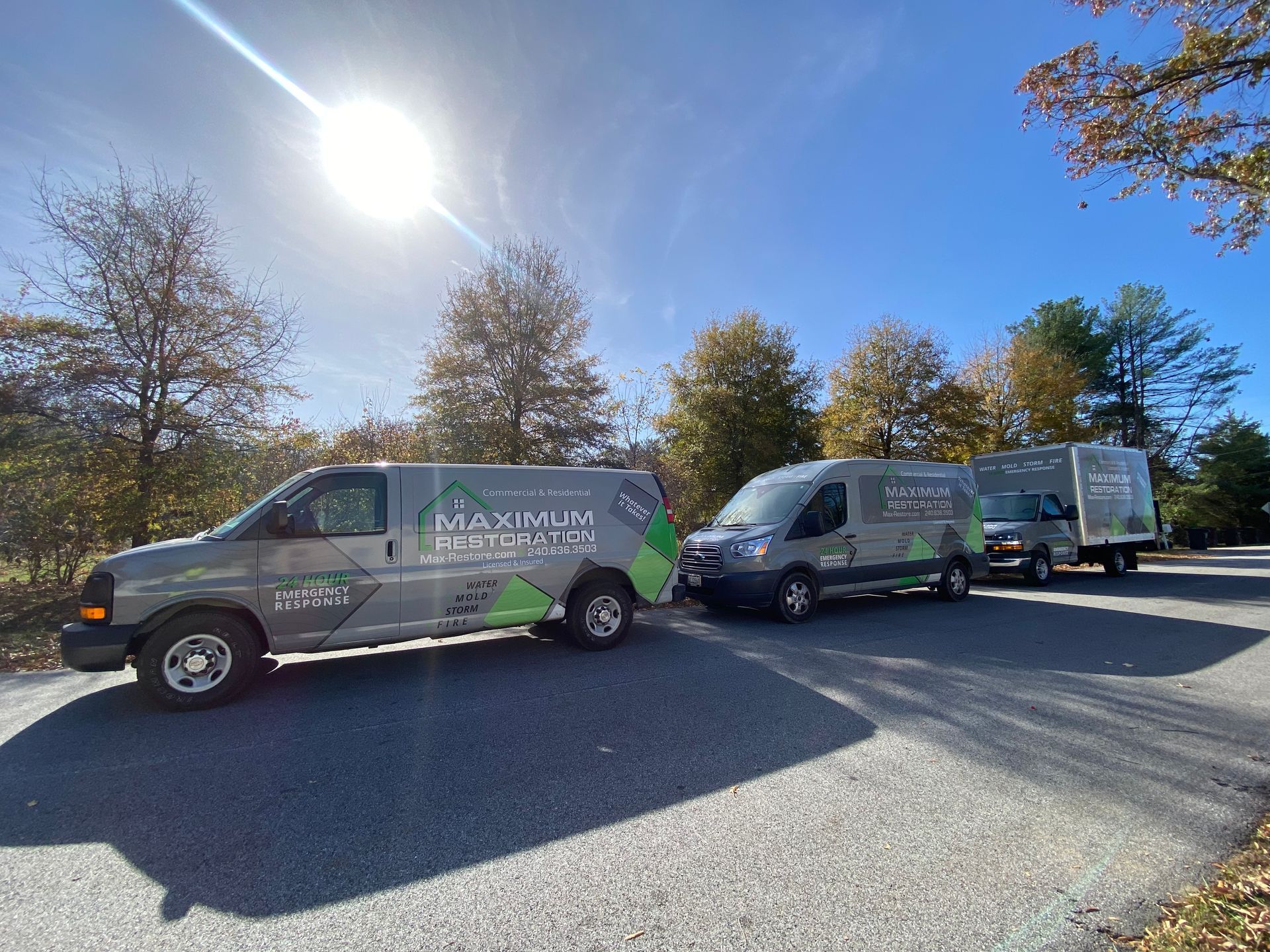 Three gray vans with company logo parked on asphalt road under a sunny, blue sky.