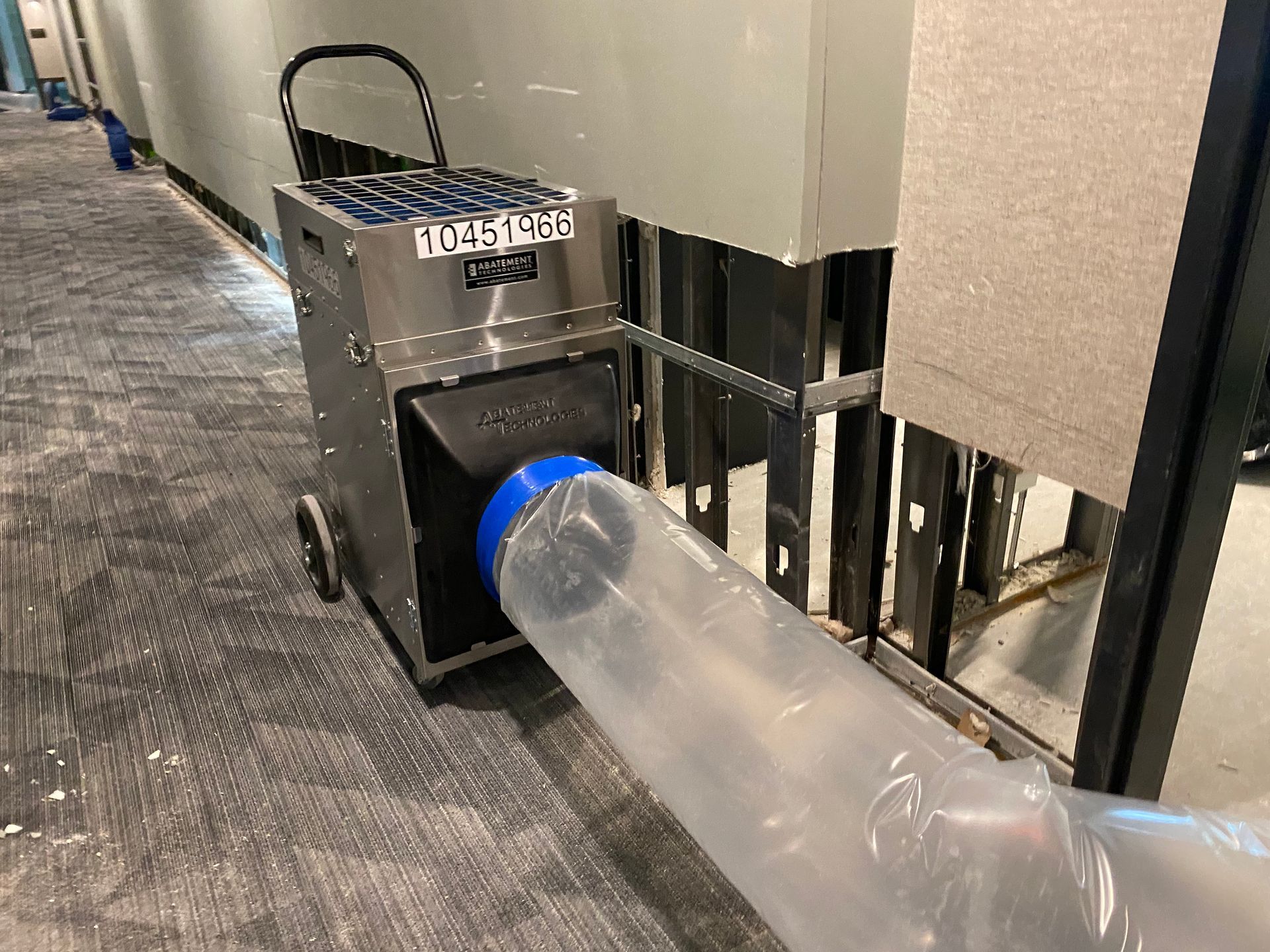 A dehumidifier on wheels is drying out a wall cavity in a commercial space.