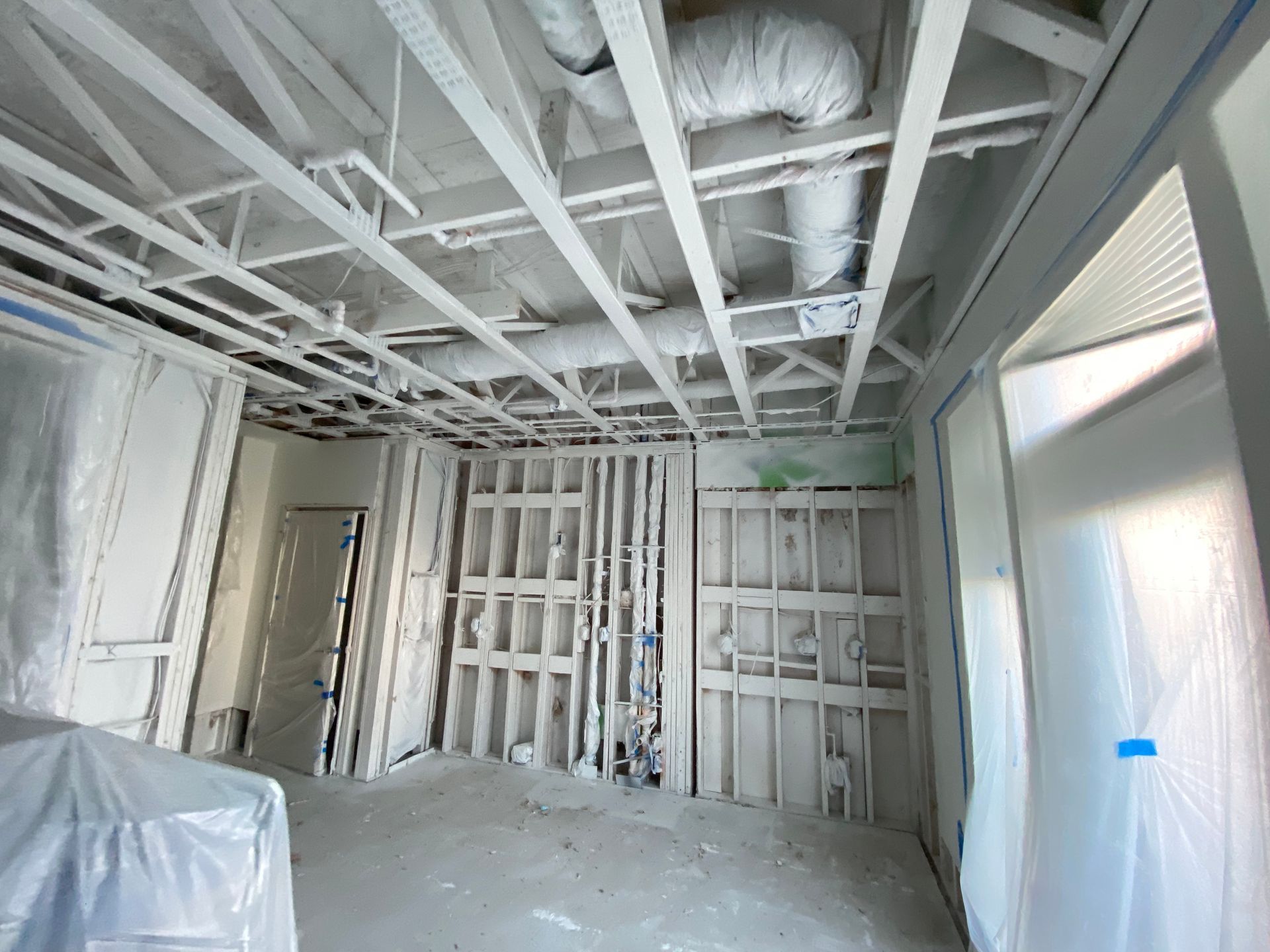 Interior view of a room under construction, with exposed wooden beams, ductwork, and partially covered walls.