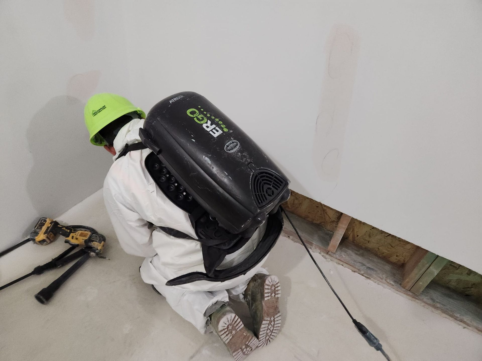 Person in protective suit using backpack-style air filtration system in a room corner.