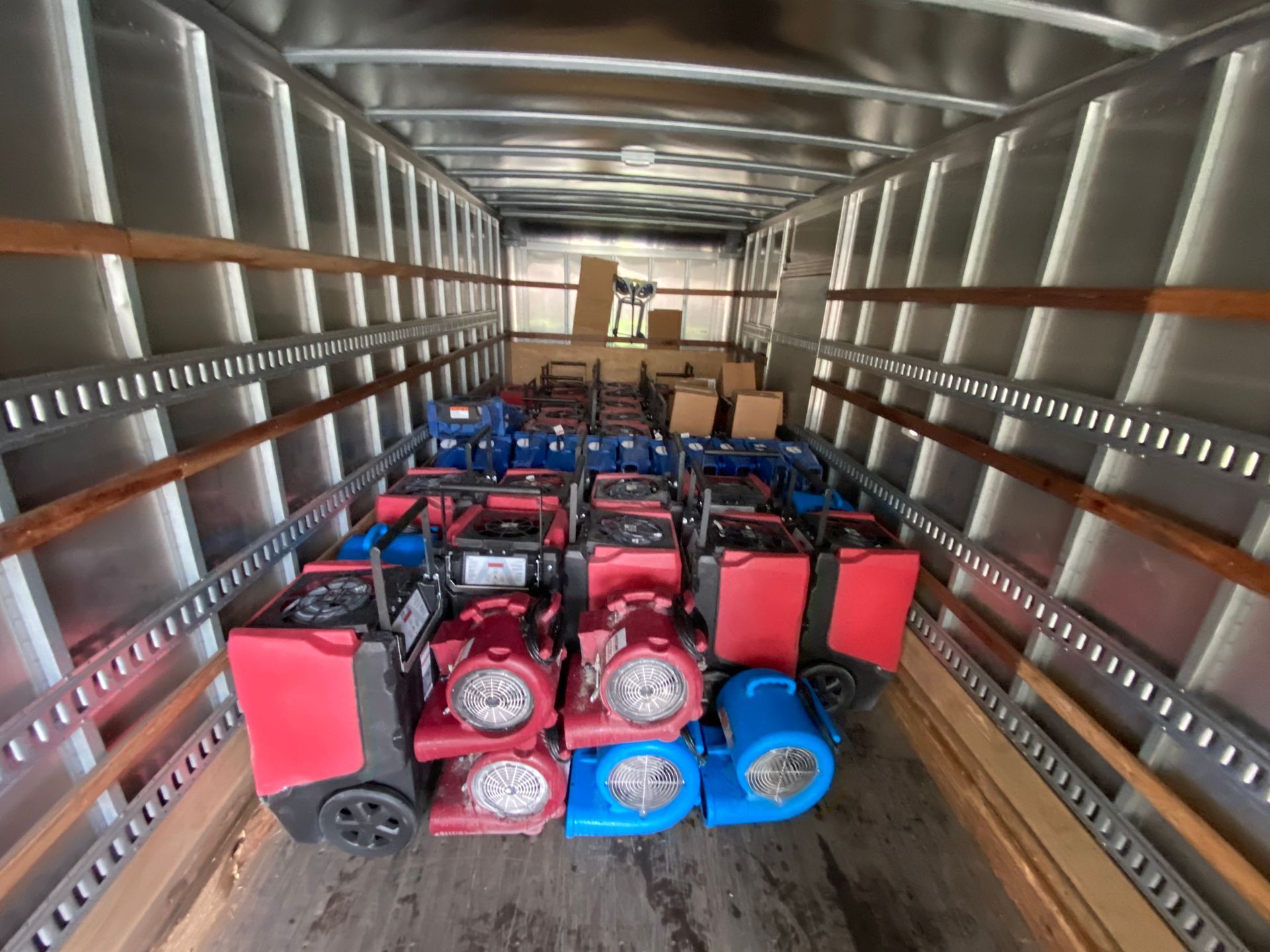 Inside a truck, numerous red, blue, and black dehumidifiers are stacked, ready for transport.