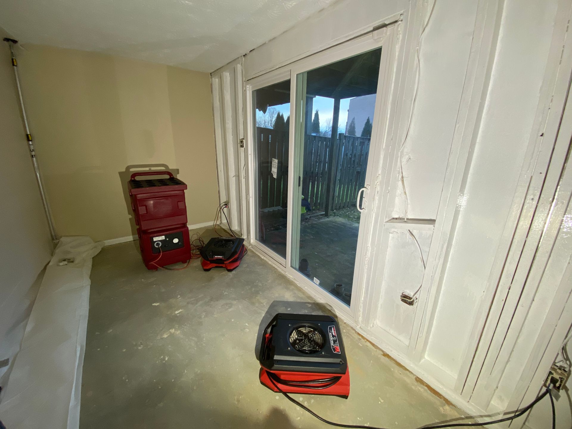 Room with sliding glass door and three red dehumidifiers; moisture restoration in progress.