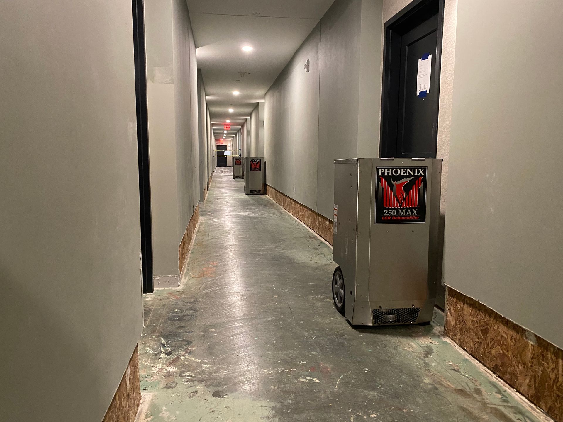 A long, narrow hallway with gray walls, a concrete floor, and several box-shaped robots.