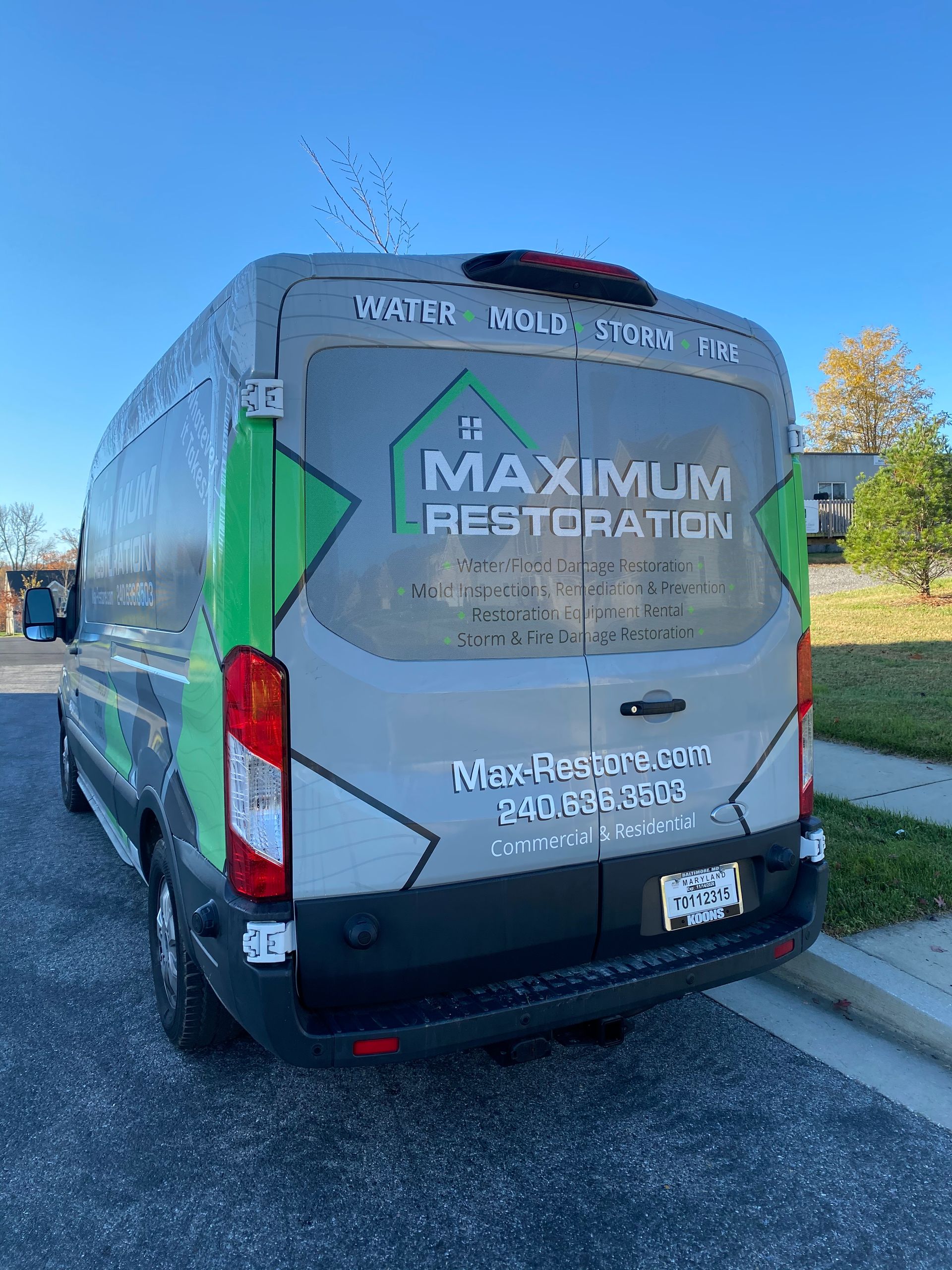 A gray van with the Maximum Restoration logo parked on a street under a blue sky.