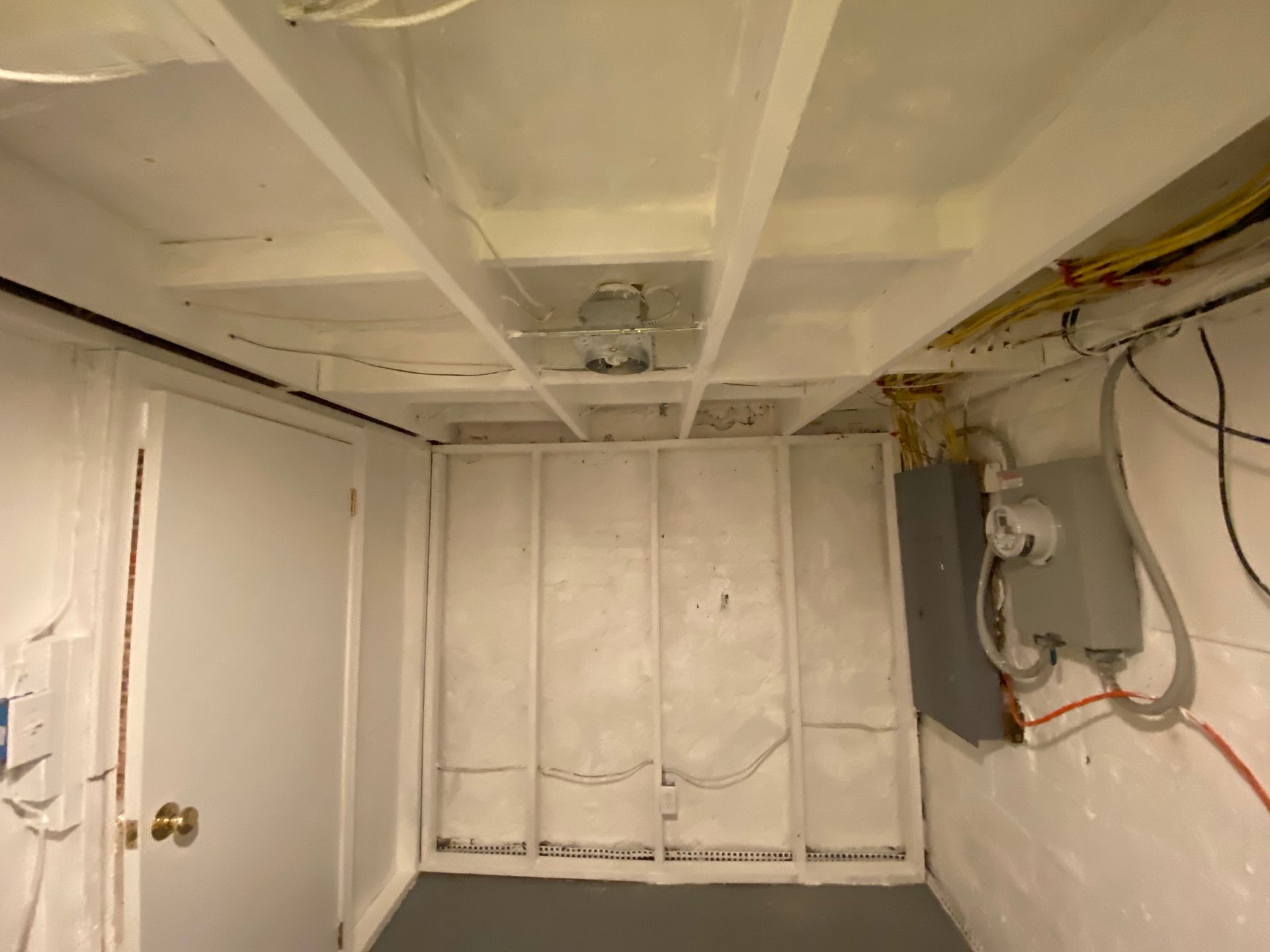 Basement interior with exposed ceiling beams and a partial unfinished wall with wiring and electrical box.