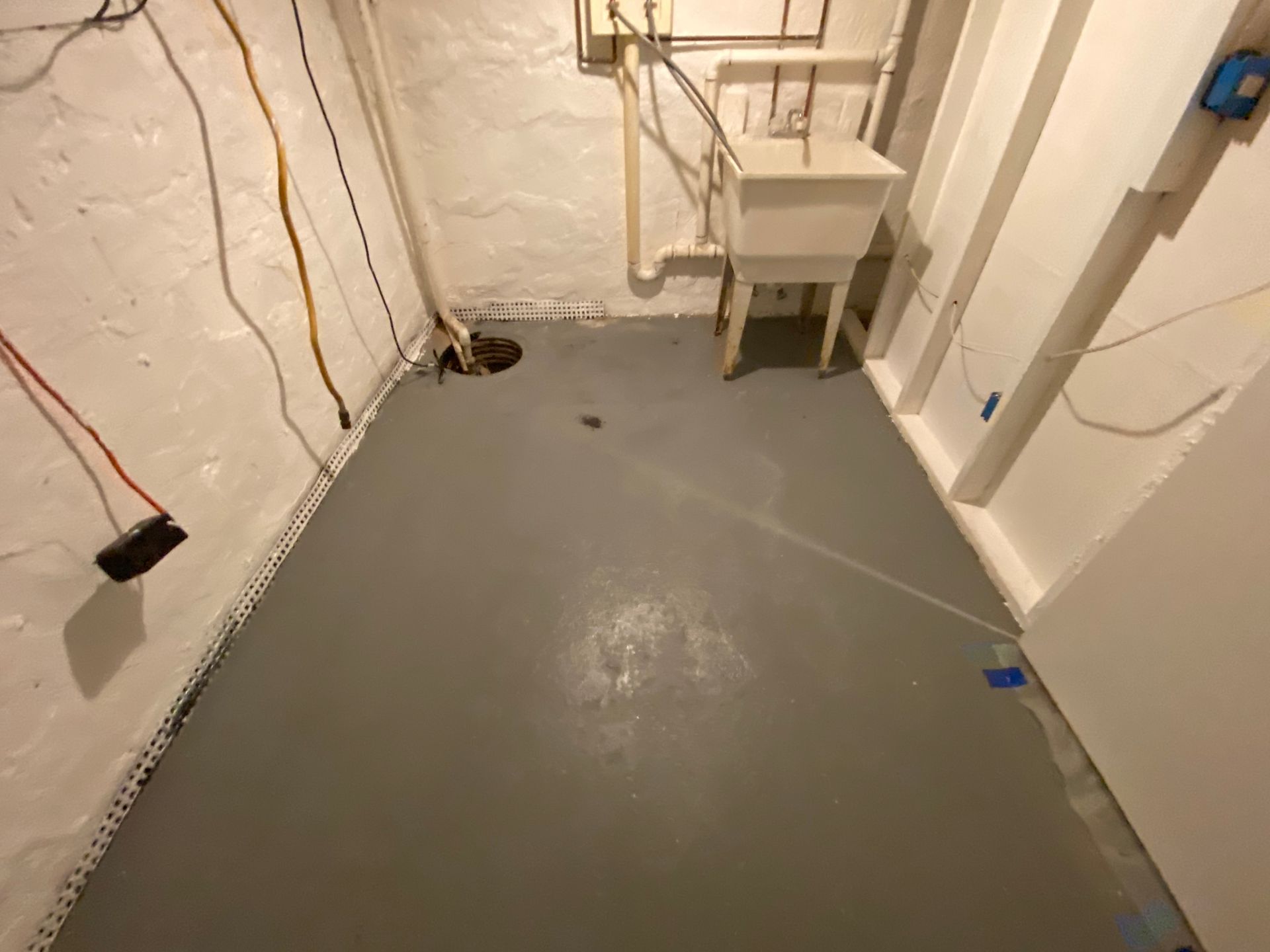 Gray painted basement floor with white walls, utility sink, and electrical wiring.