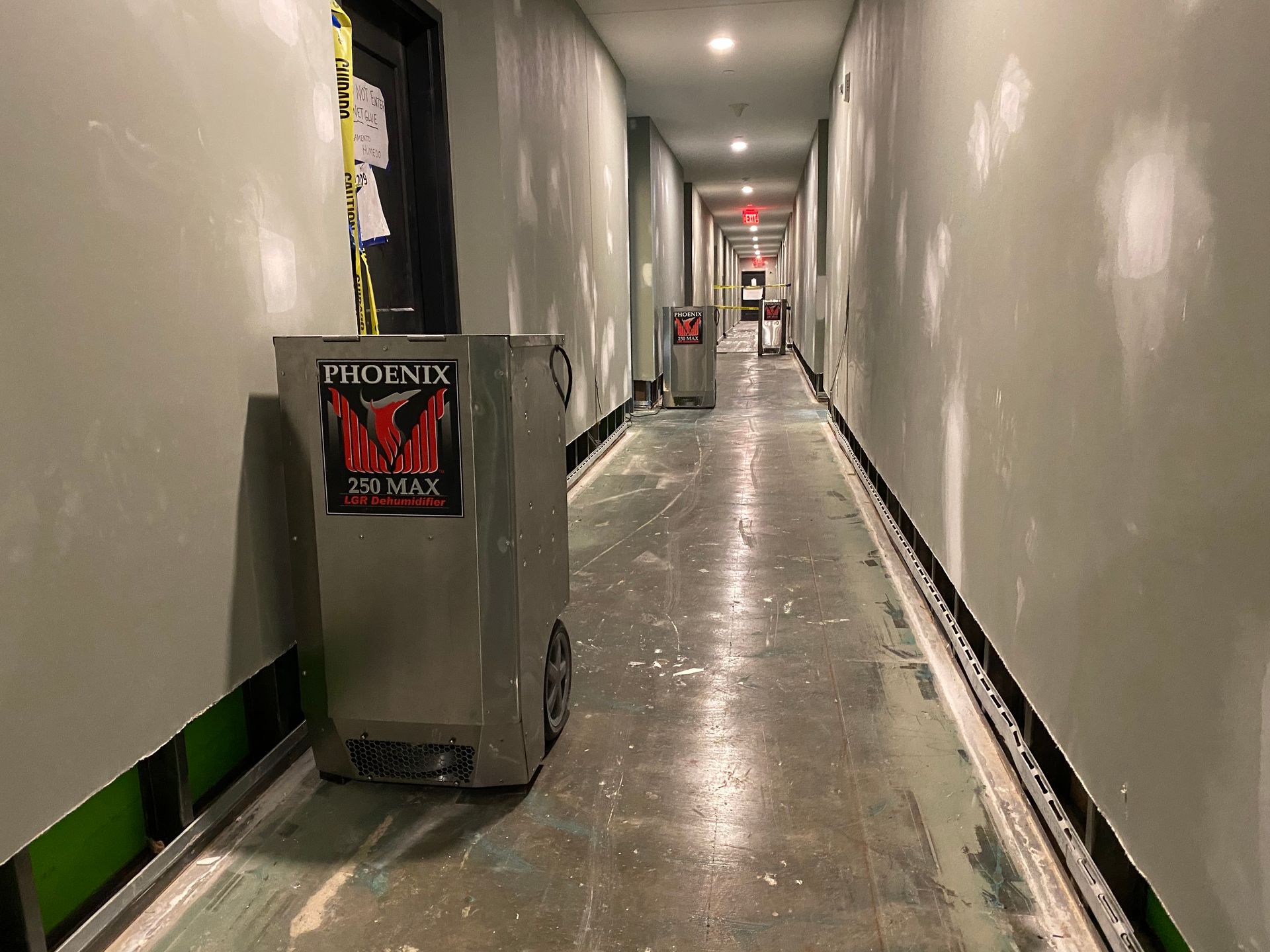 A long hallway with several gray trash cans, one close, two further down. Walls are unfinished.