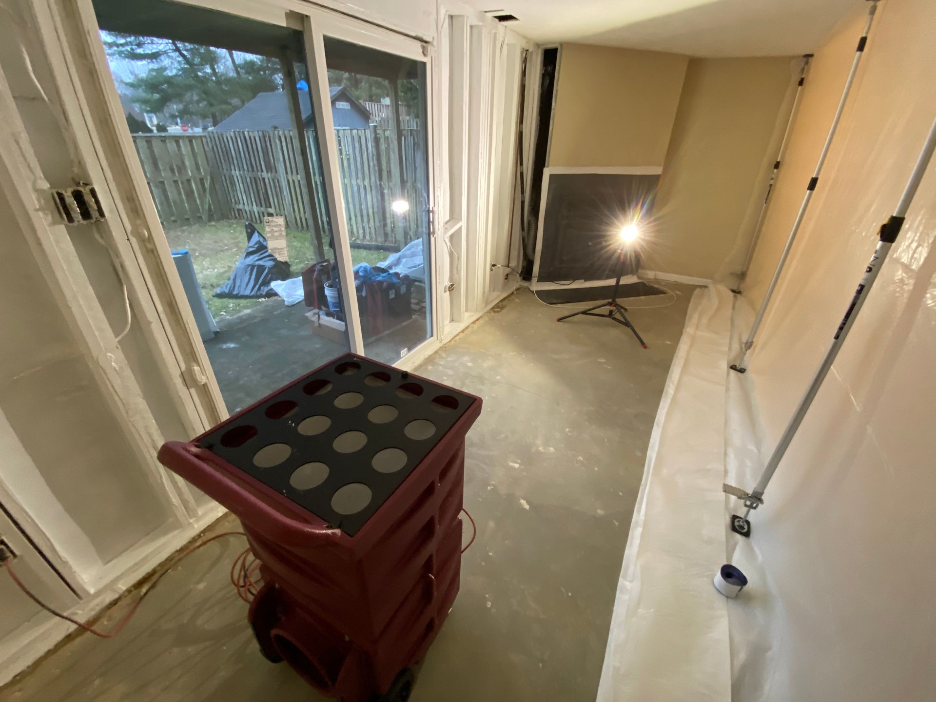 Red cart in room with plastic sheeting; sliding glass door to yard. Lighting setup.