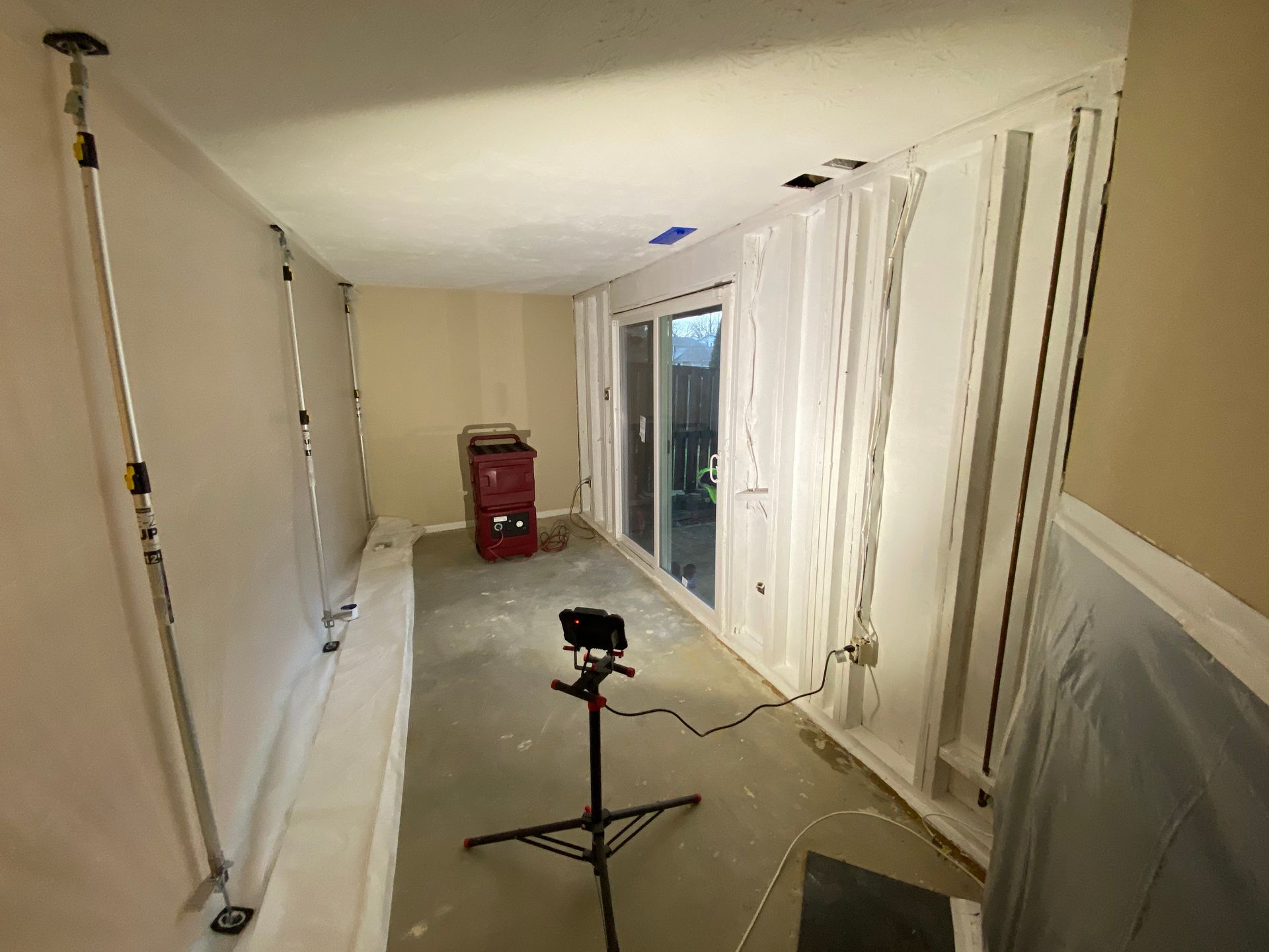 Room with protective sheeting and equipment, including a tripod-mounted light, likely during renovation or construction.