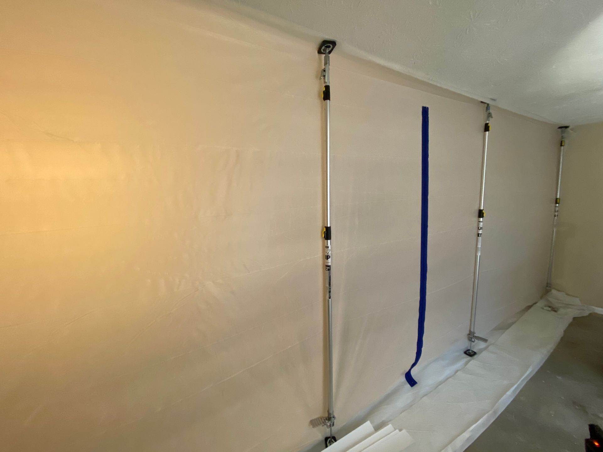 Plastic sheeting on walls secured with poles, masking tape, protecting the room during construction.