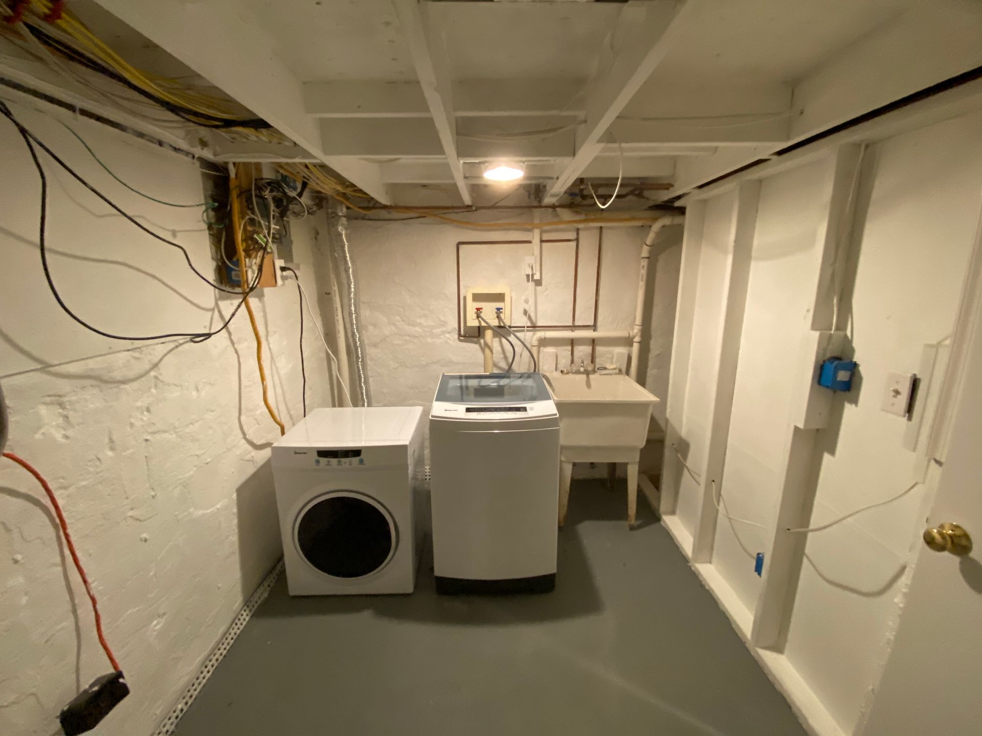 Laundry room with a washing machine, dryer, and utility sink against white walls.