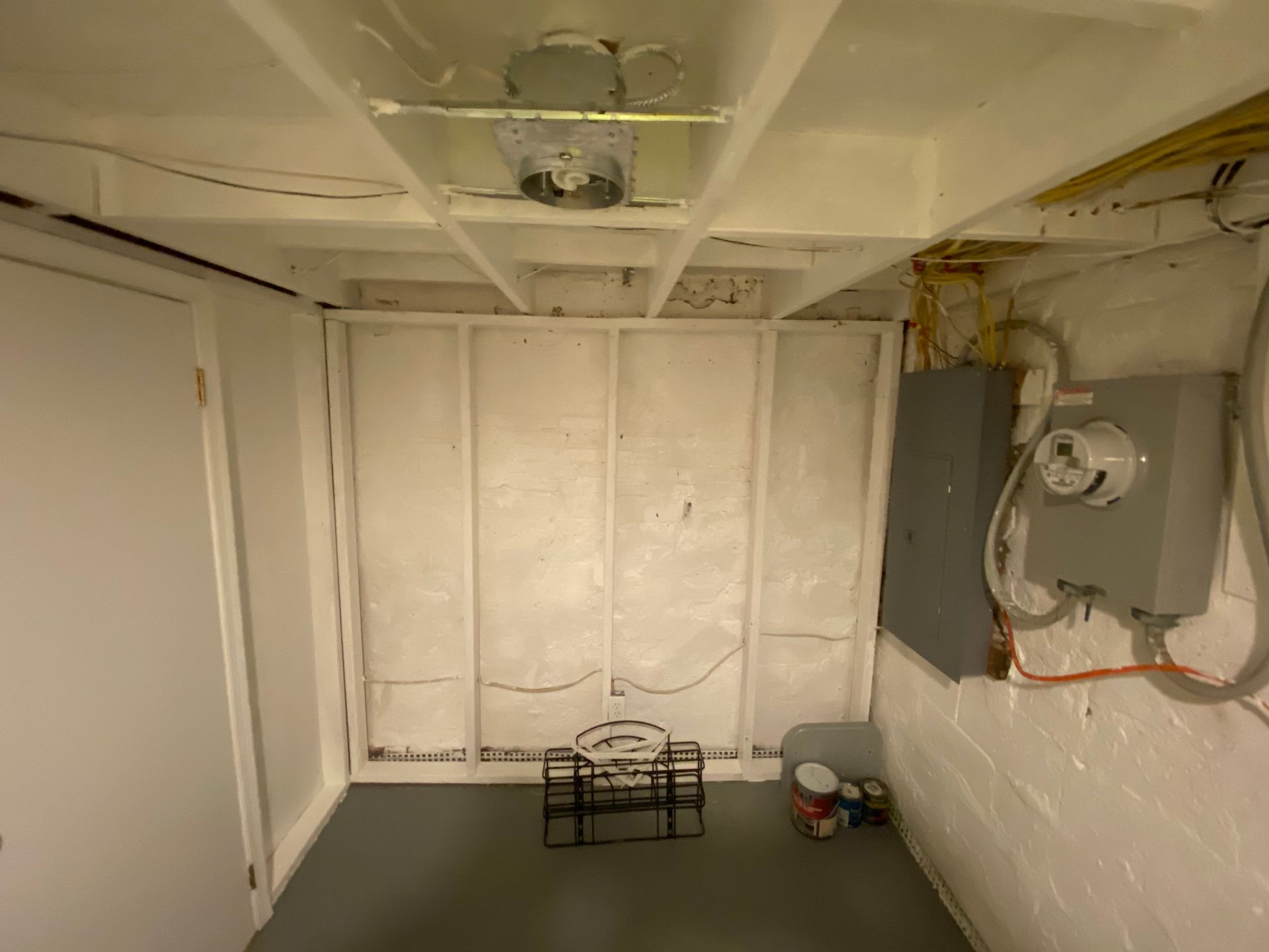 Basement room with exposed framing, electrical panel, and door. Gray and white colors dominate the space.