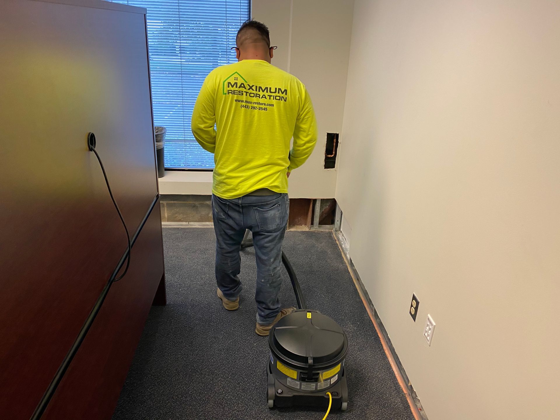 Person in yellow shirt vacuums carpet in office.