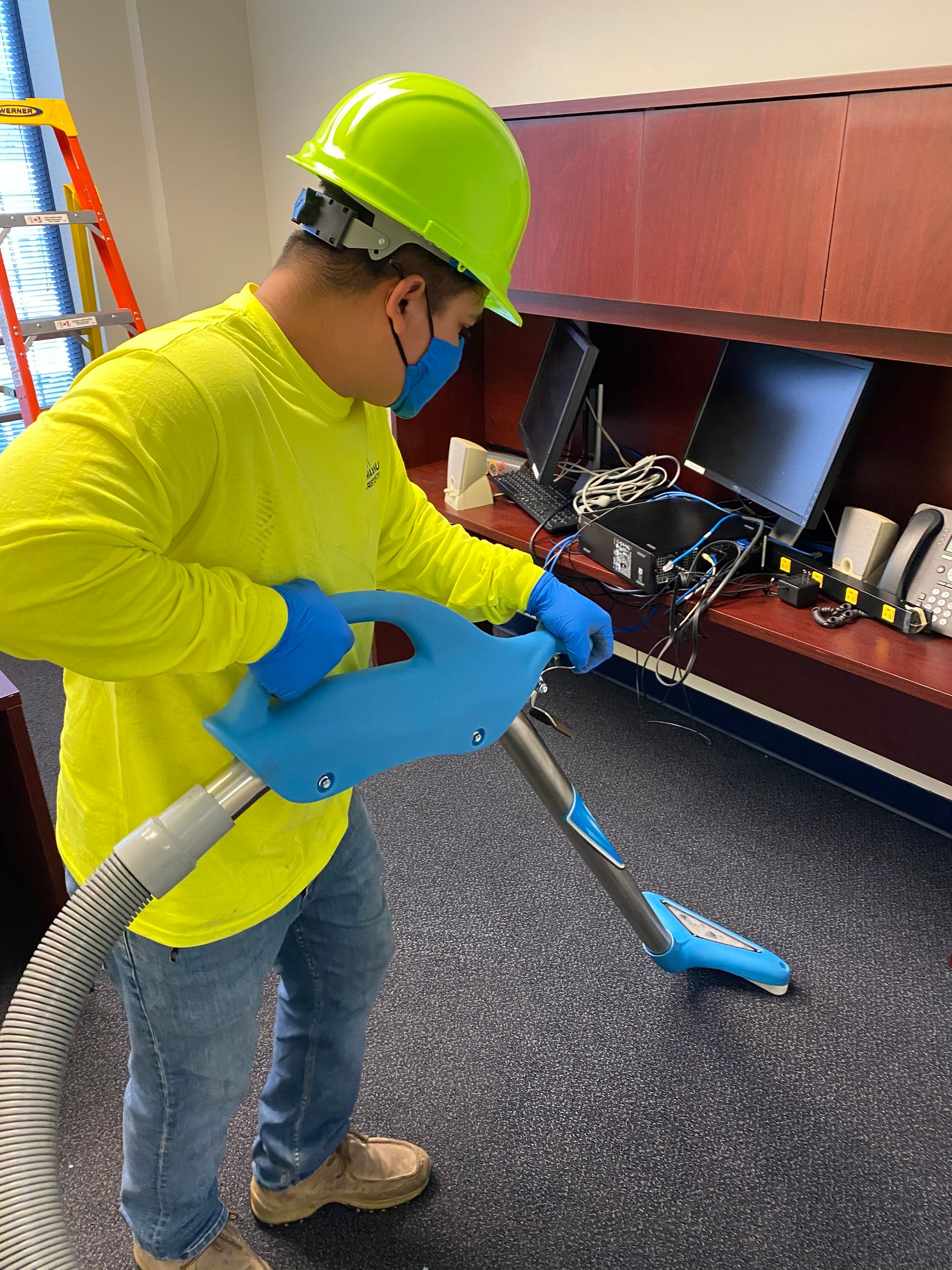 Person in protective gear vacuums a carpeted office floor.