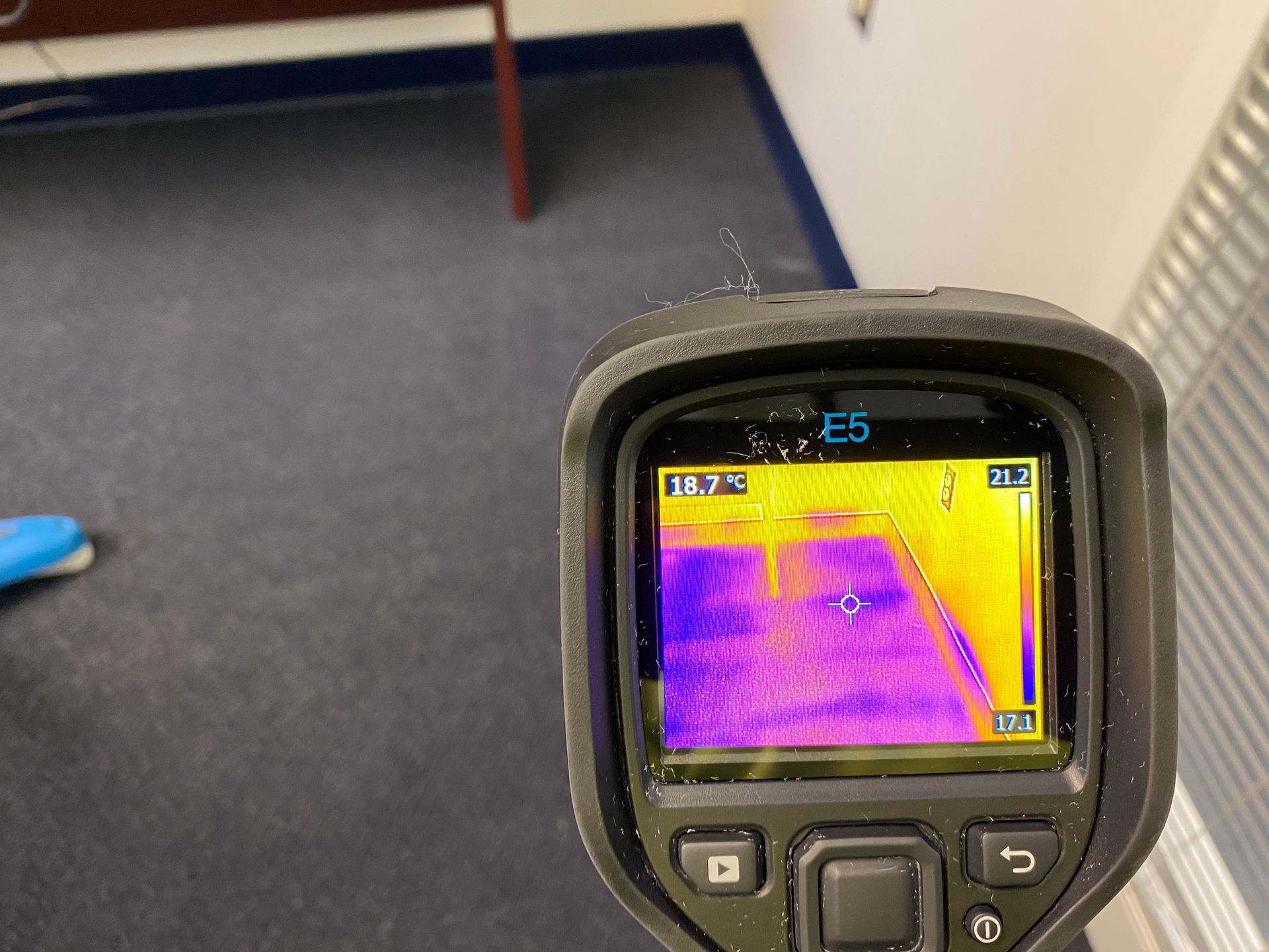 Thermal camera displaying a purple-yellow temperature reading of a dark carpeted floor, likely inspecting for leaks.