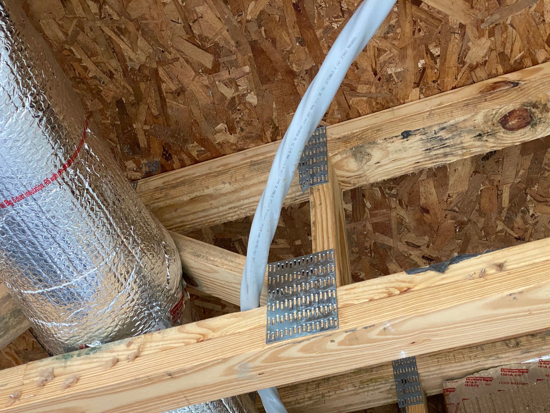 Wooden roof rafters with ductwork and a cable secured by metal plates.