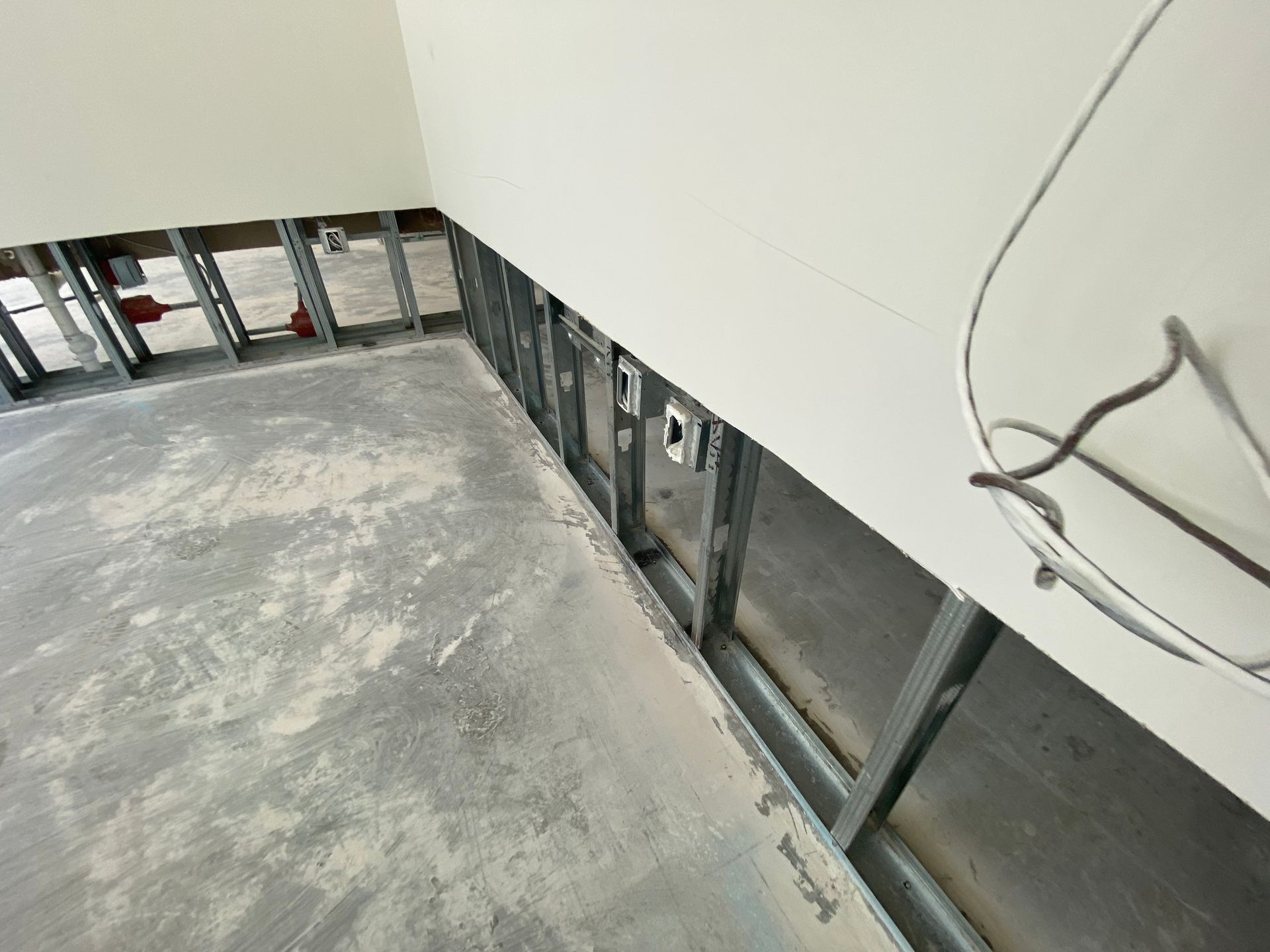 Interior room under construction, with exposed metal framing, unfinished walls, and concrete floor.