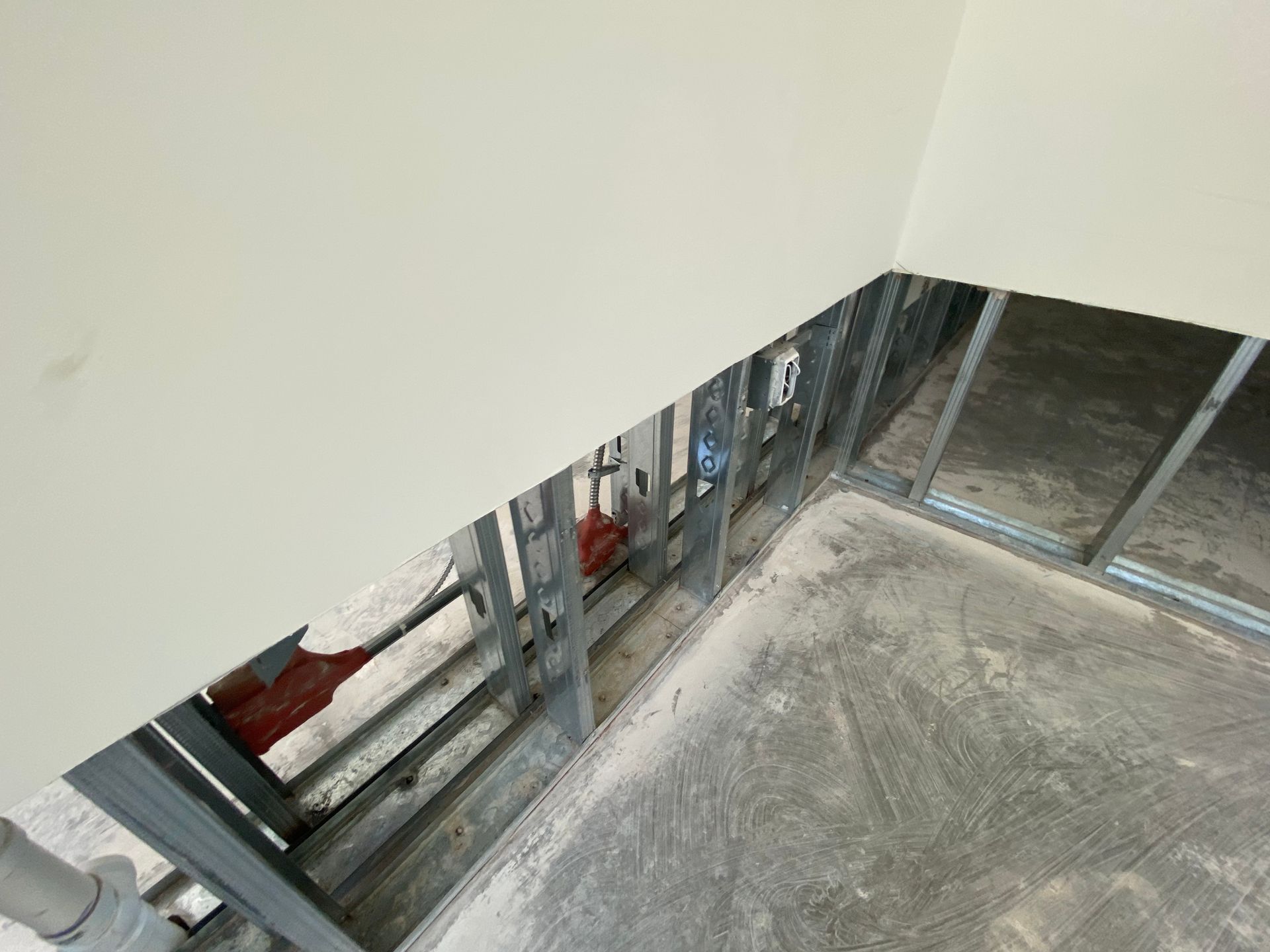 Exposed metal studs in a partially constructed room. Red pipes and electrical outlets are visible within the wall frame.