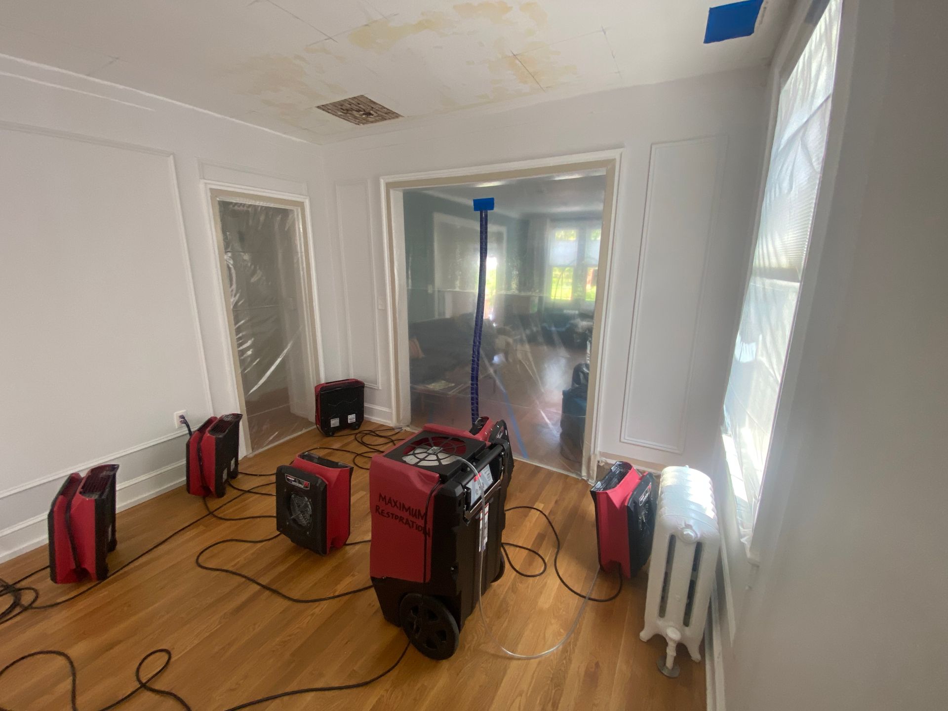 Room with water damage undergoing restoration. Dehumidifiers and plastic sheeting are present.