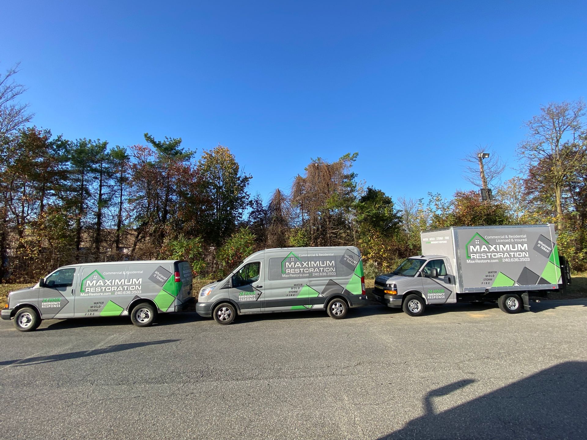 Three gray work vans parked, each with the same green and black company logo against a blue sky.